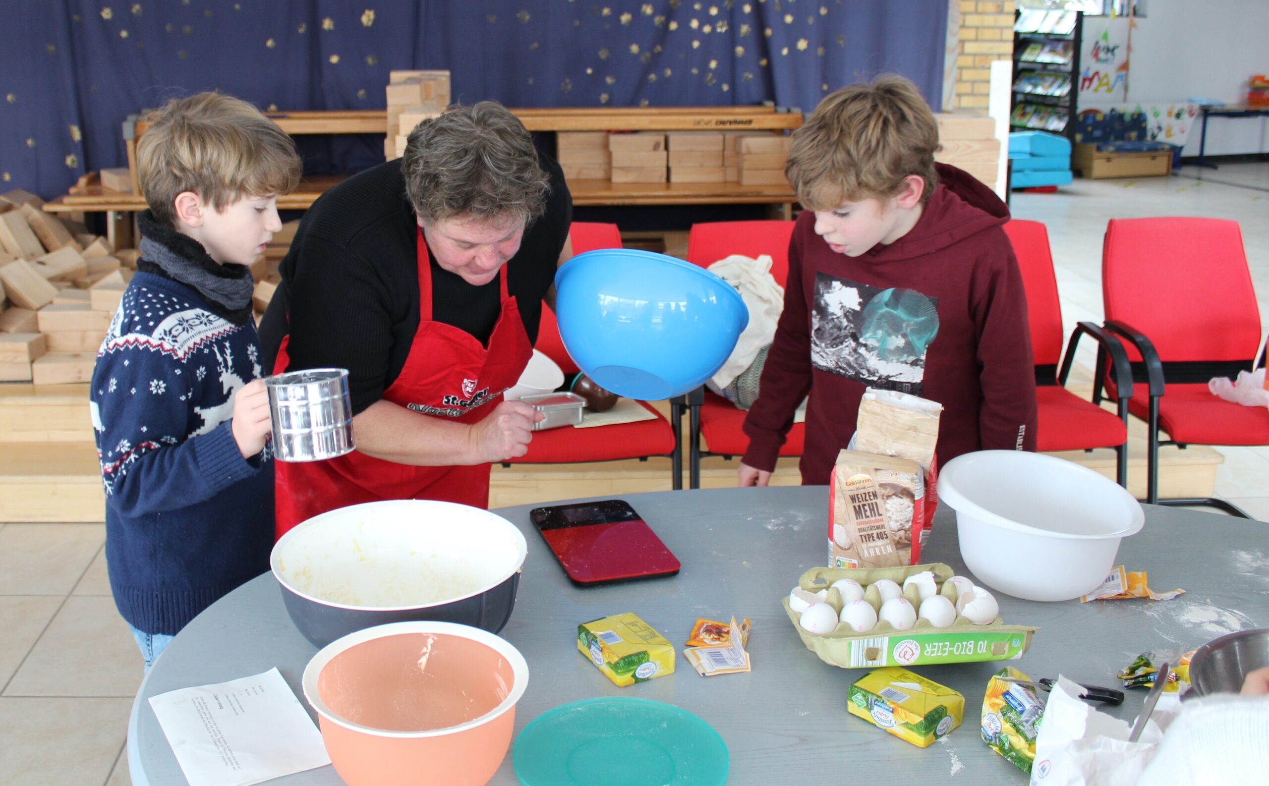 Eine Mutter und zwei Jungen aus einer dritten Klasse bereiten wiegen gerade die Zutaten für einen Teig ab.