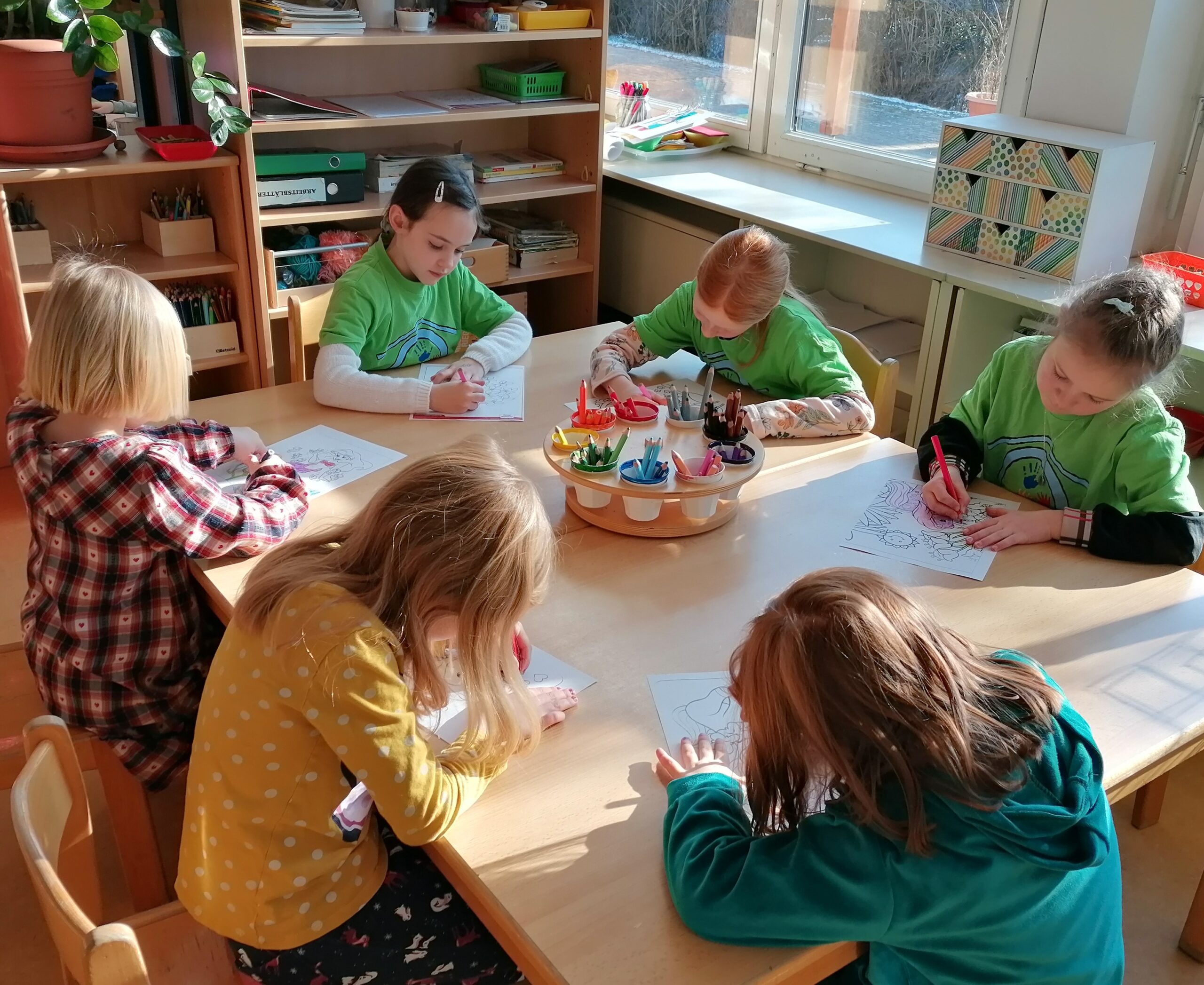 Schul- und Kindergartenkinder malen an einem Tisch.