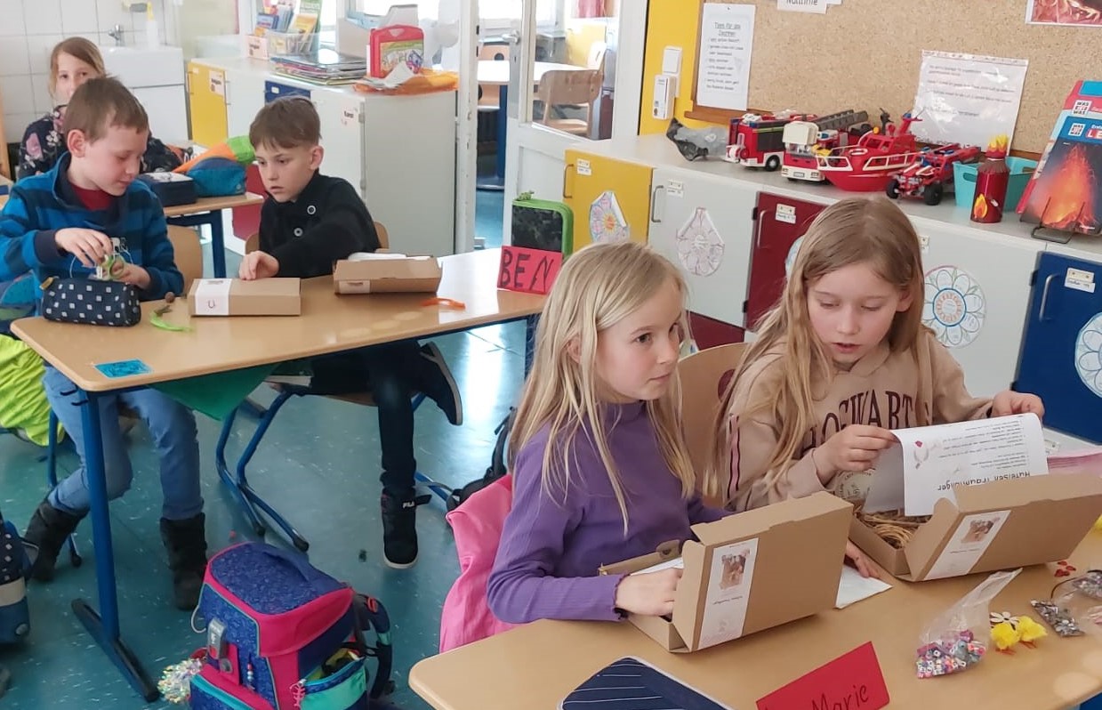 Grundschulkinder sitzen in einem Klassenzimmer und basteln ein Glückshufeisen.