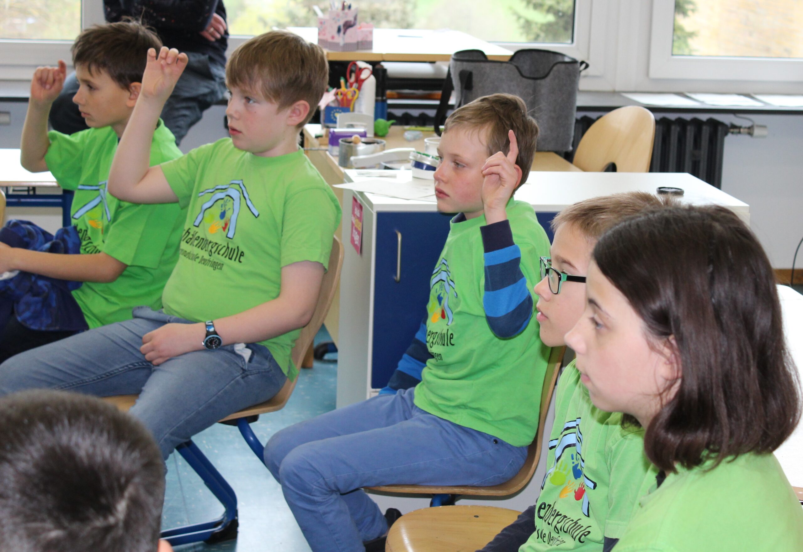 Fünf Kinder in grünen Schul-T-Shirts folgen konzentriert der Vorstellung.