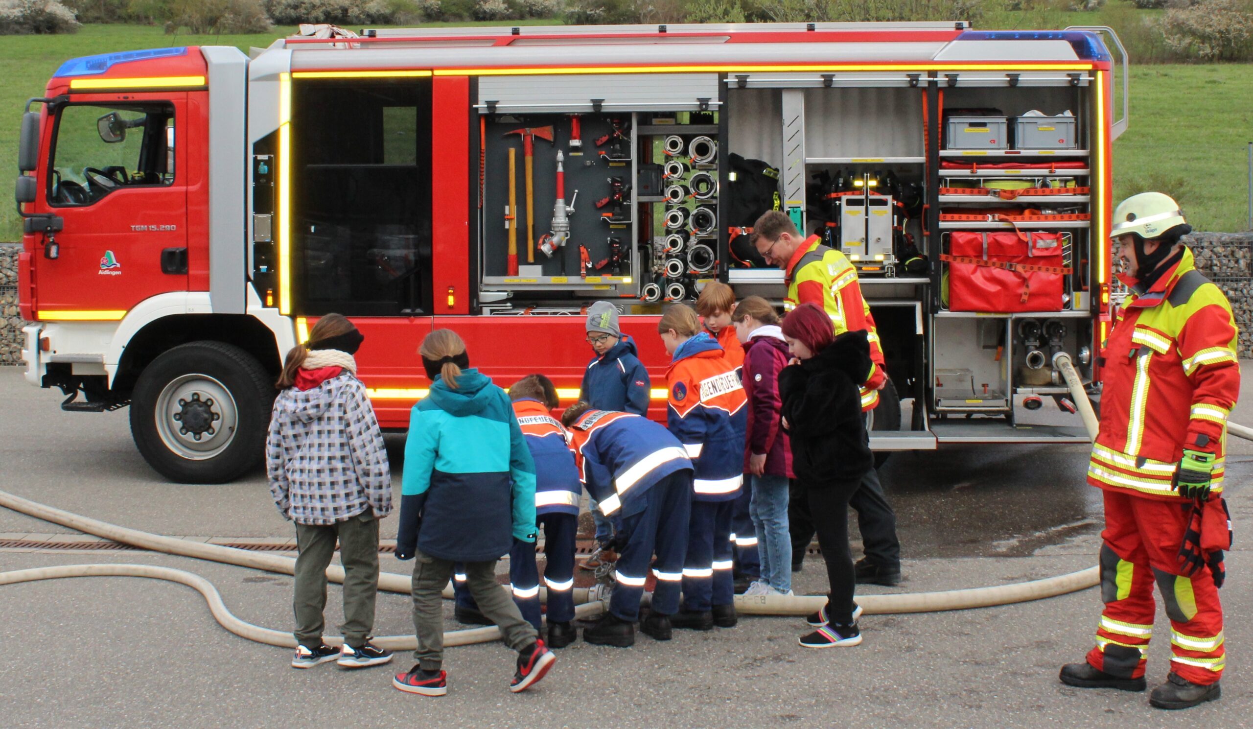 Kinder einer Schulklasse stecken Feuerwehrschläuche zusammen.