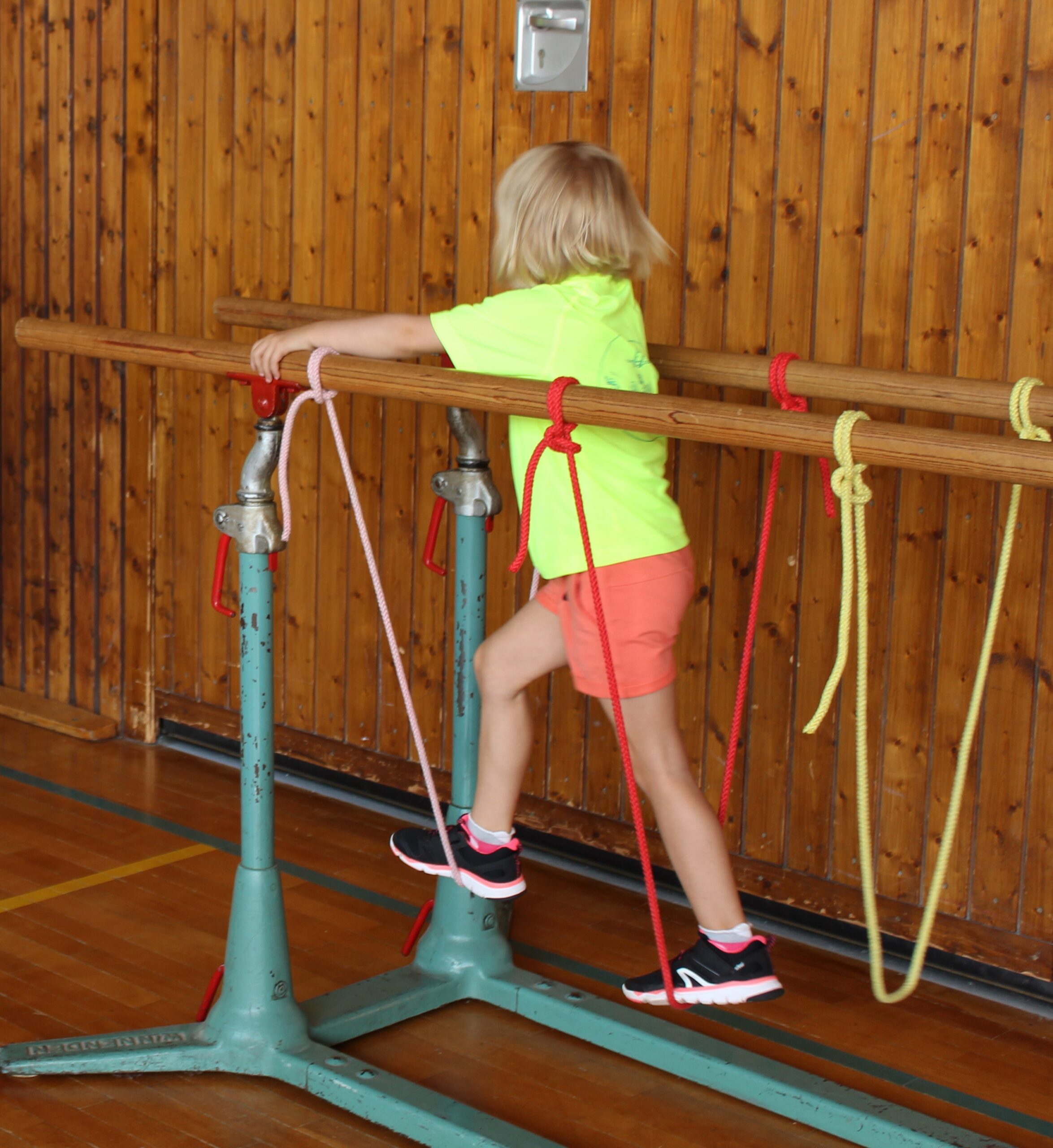 Ein Kindergartenkind balanciert über die Hängebrücke aus Seilen an einem Barren.