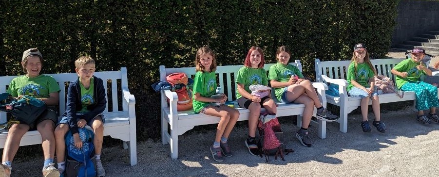 Schulkinder sitzen in ihren Schul-T-Shirts auf einer Bank und machen Pause.