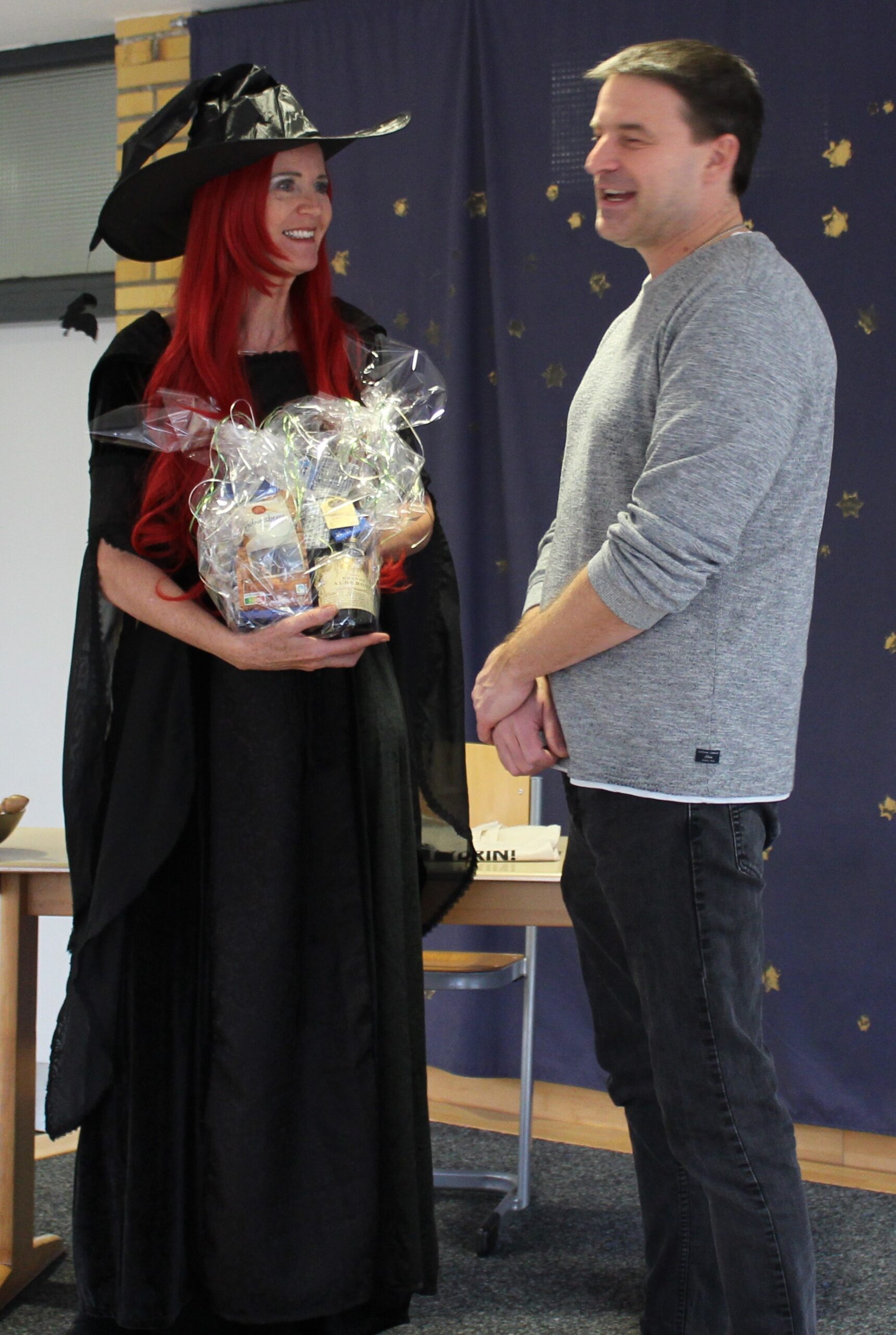 Die als Hexe verkleidete Rektorin überreicht Herrn Vetter ein Geschenk als Dankeschön.