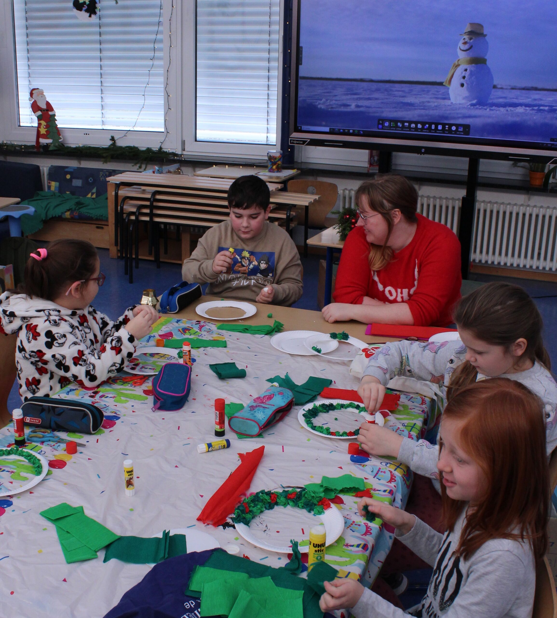 Kinder sitzen in einem Klassenzimmer um Tische und basteln aus Papier einen Weihnachtskranz.