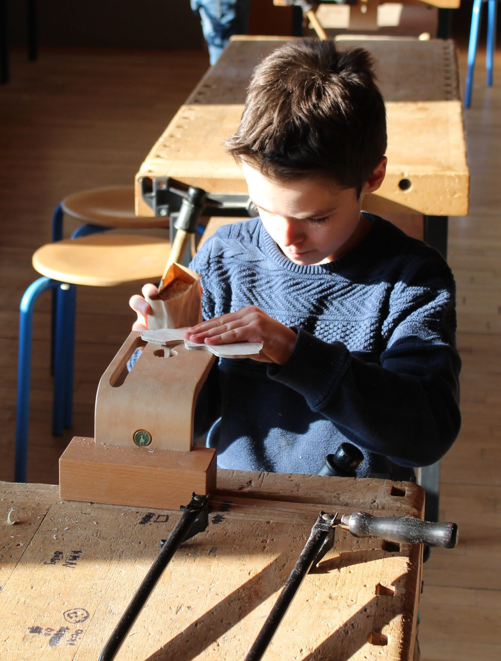 Ein Junge bearbeitet mit Schleifpapier sein ausgesägtes Holzstück.