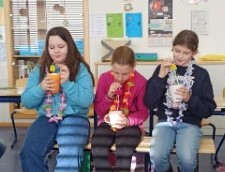 Drei Mädchen sitzen auf einer Bank in einem Klassenzimmer und trinken selbstgemixte Kindercocktails.
