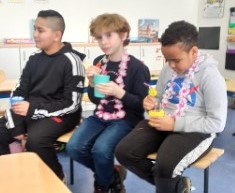 Drei Jungen sitzen auf einer Bank in einem Klassenzimmer und trinken selbstgemixte Kindercocktails.