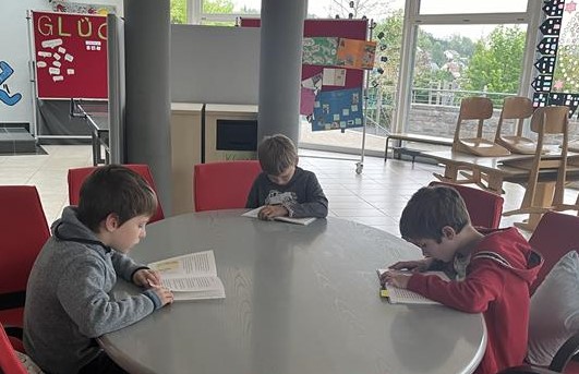 Drei Jungen sitzen um einen Tisch in der Schulaula und lesen.