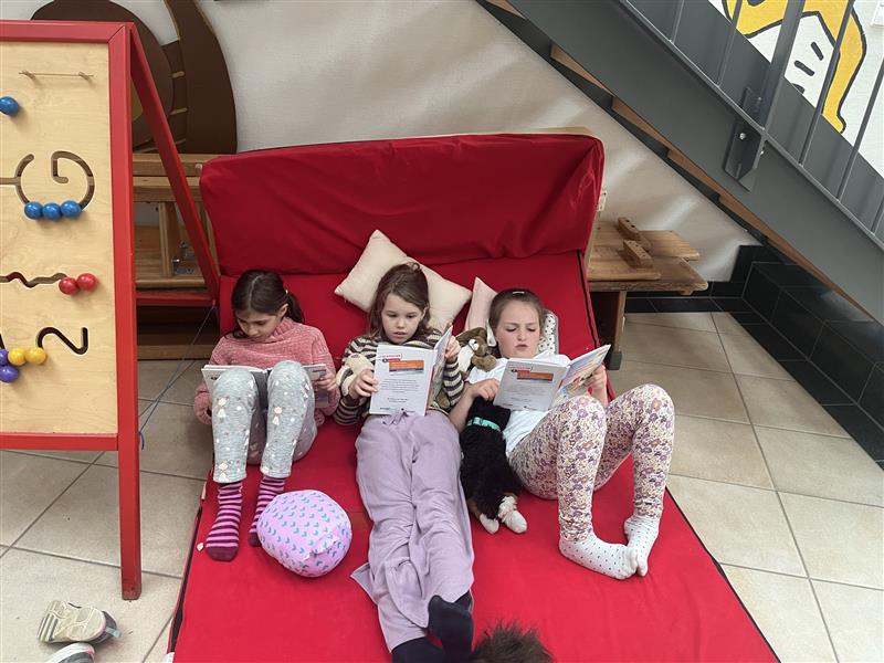 Drei Mädchen liegen auf einer Matte und lesen.
