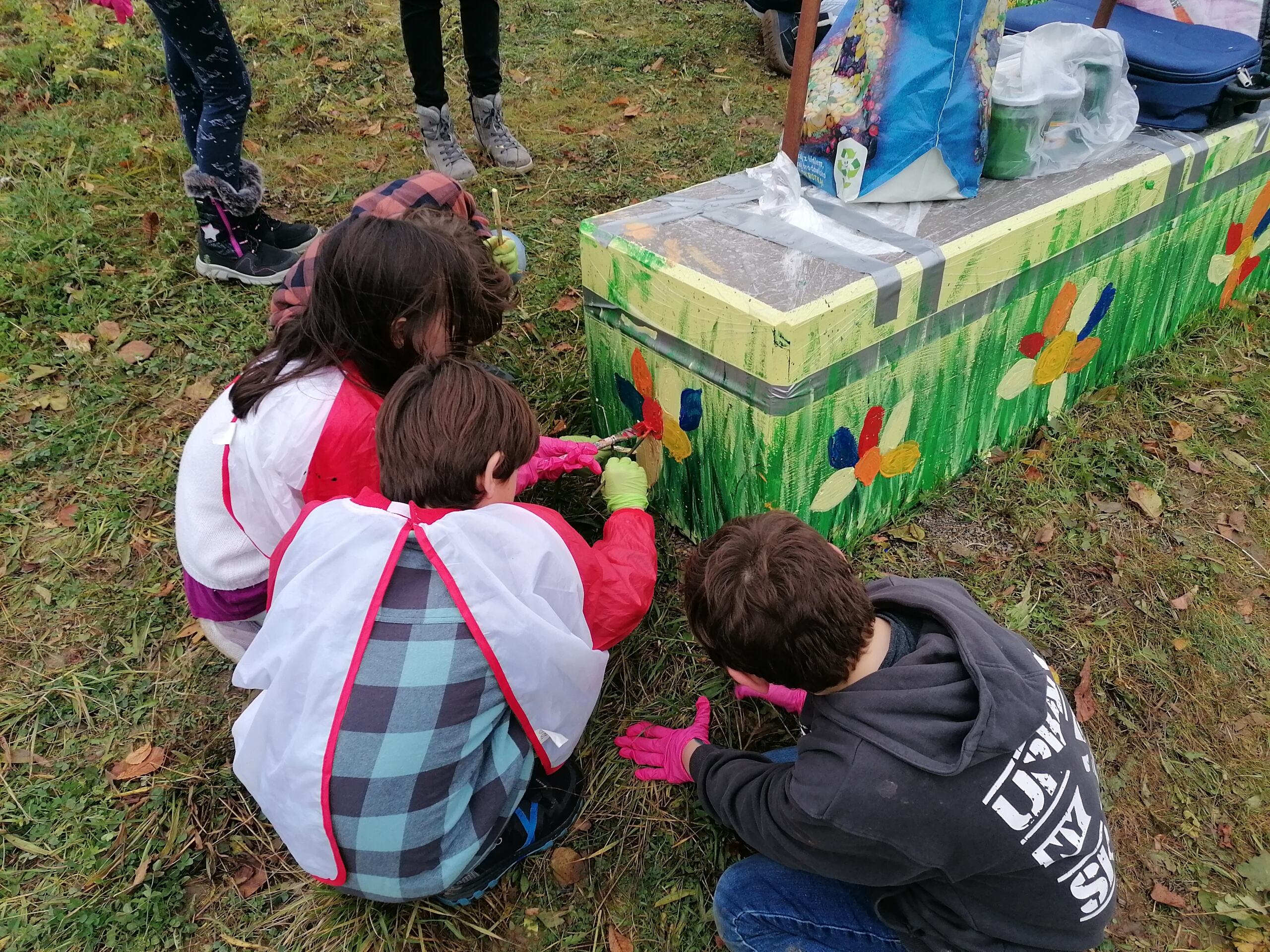 Schulkinder bemalen einen Betonsockel auf dem eine bunte Schneckenskulptur steht. 