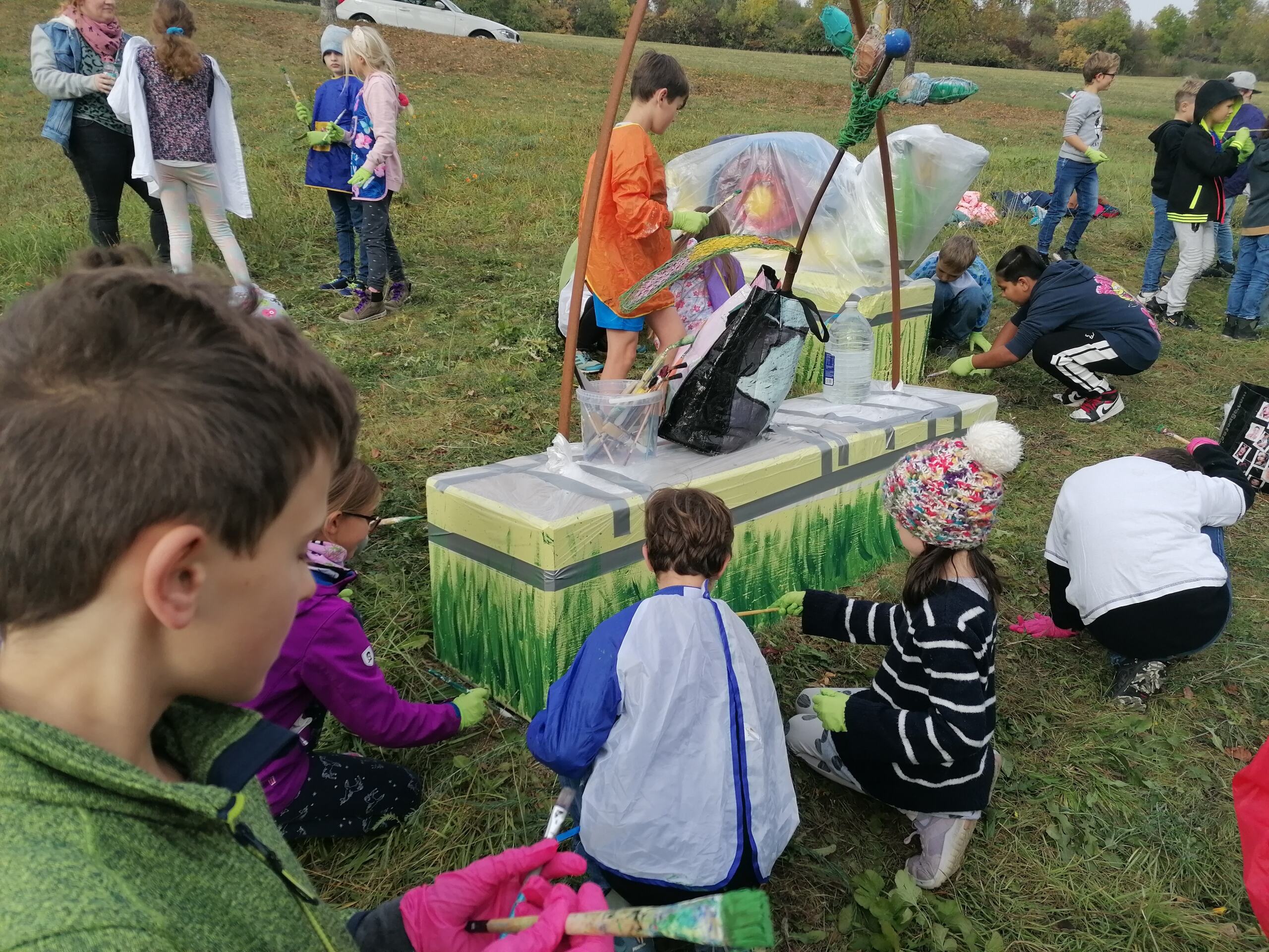 Kinder malen auf einen Betonsockel einer Schneckenskulptur eine Wiese.