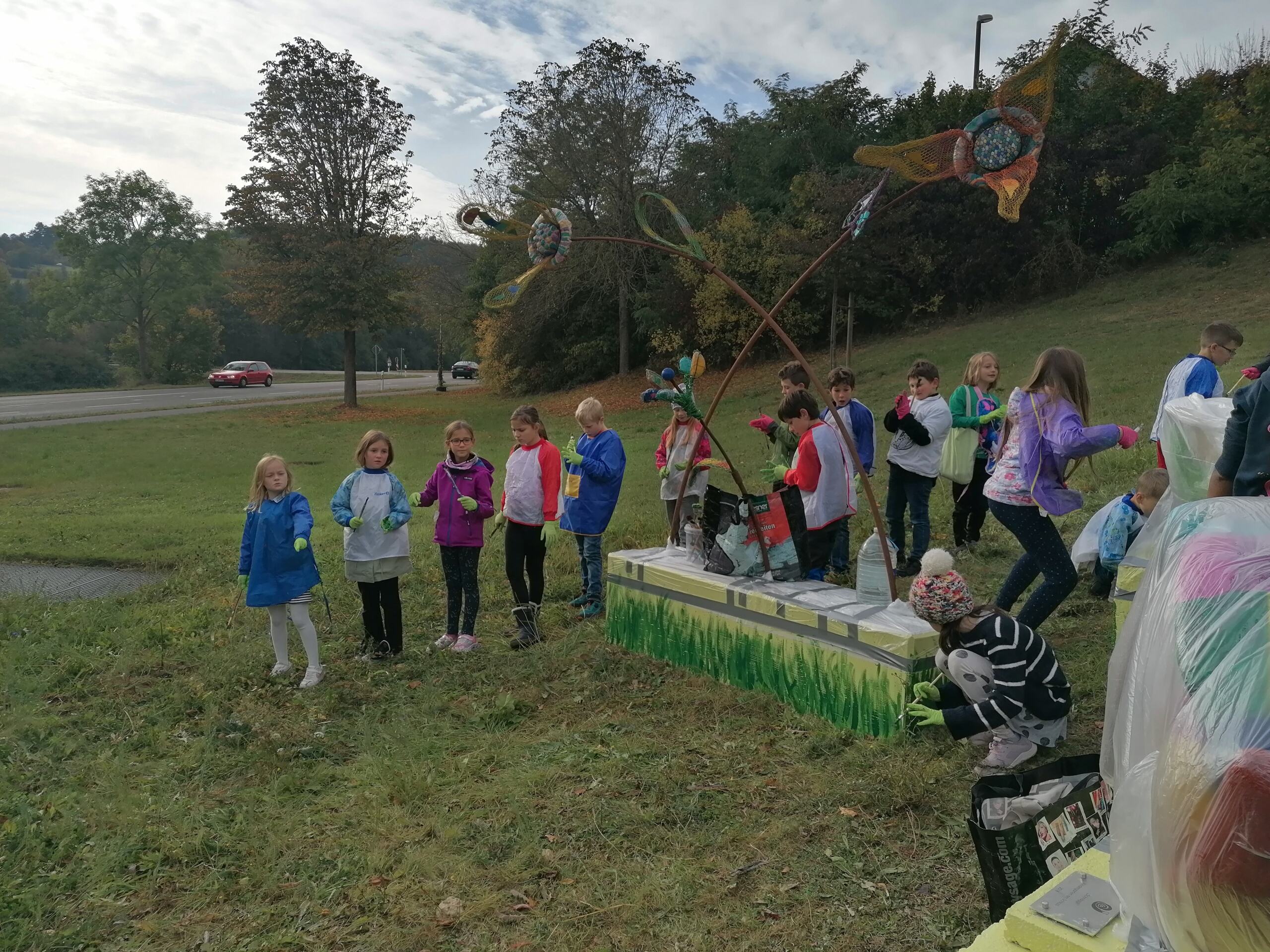 Schulkinder stehen um eine bunte Schneckenskulptur auf einer Wiese.