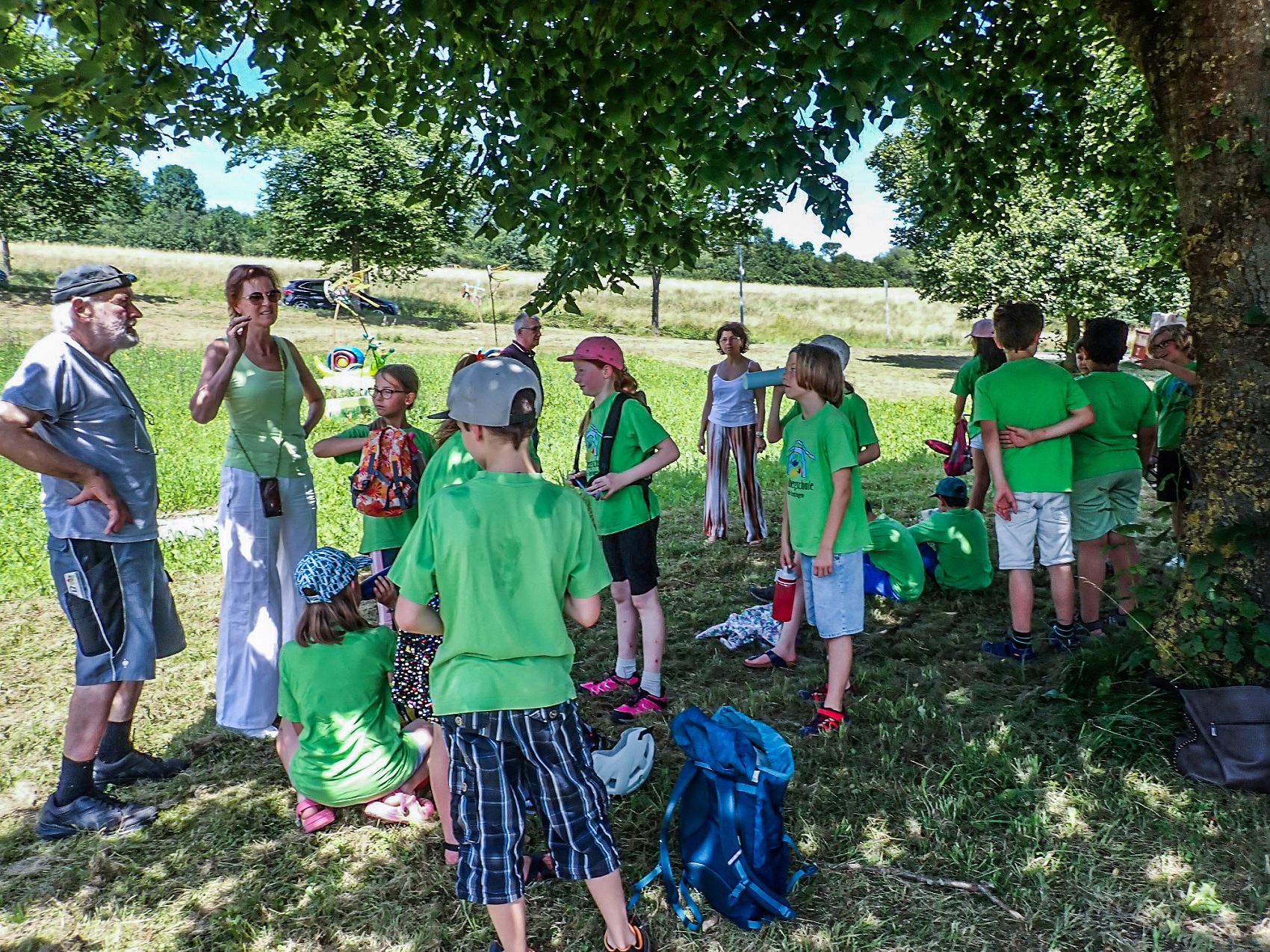 Unter einem Baum stehen im Schatten Kinder einer Schulklasse mit ihrer Rektorin.