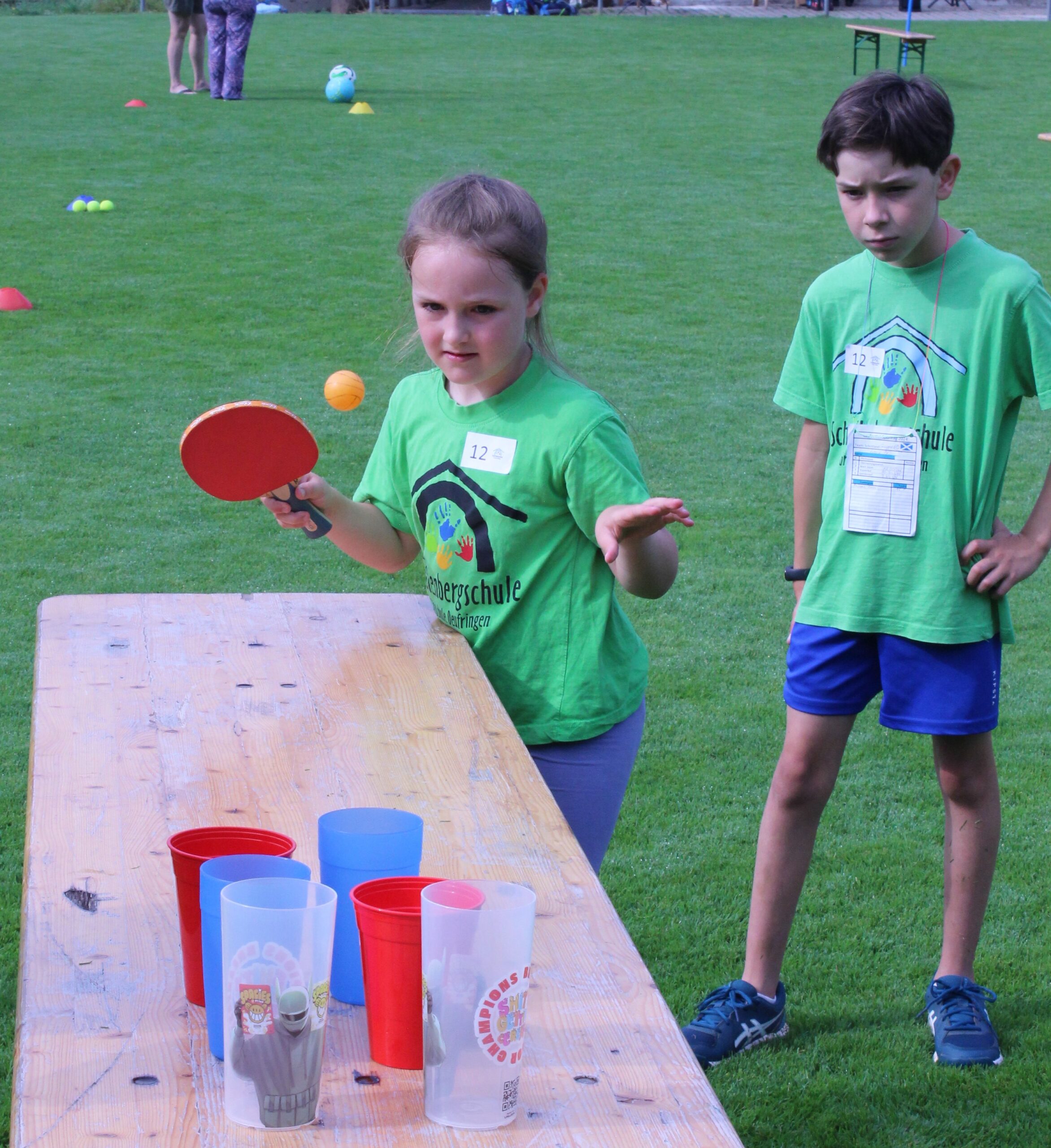 Ein Mädchen spielt einen Tischtennisball auf einer Platte und versucht ihn in Becher zu treffen.