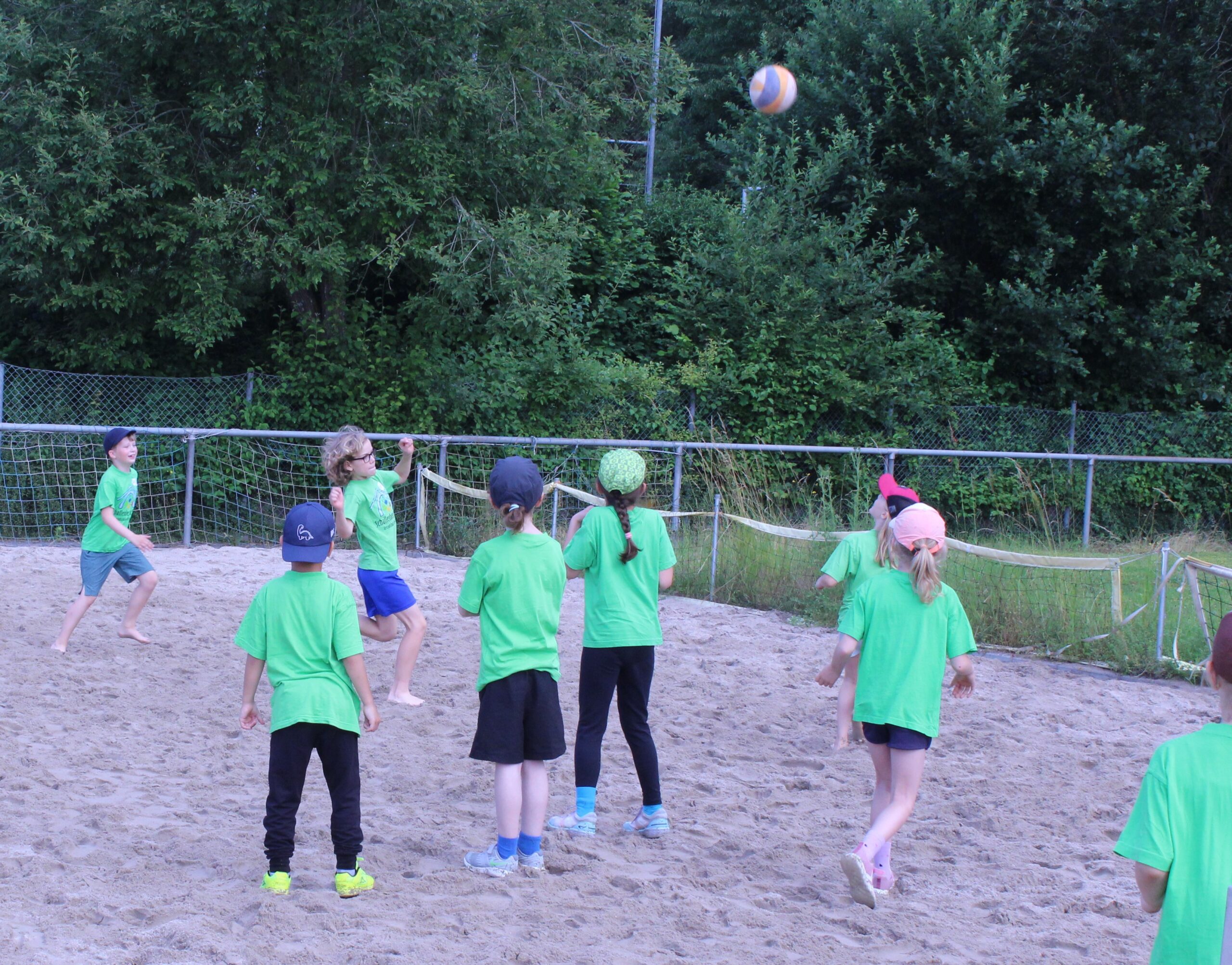 Kinder spielen Beach Volleyball auf einem Sandplatz.