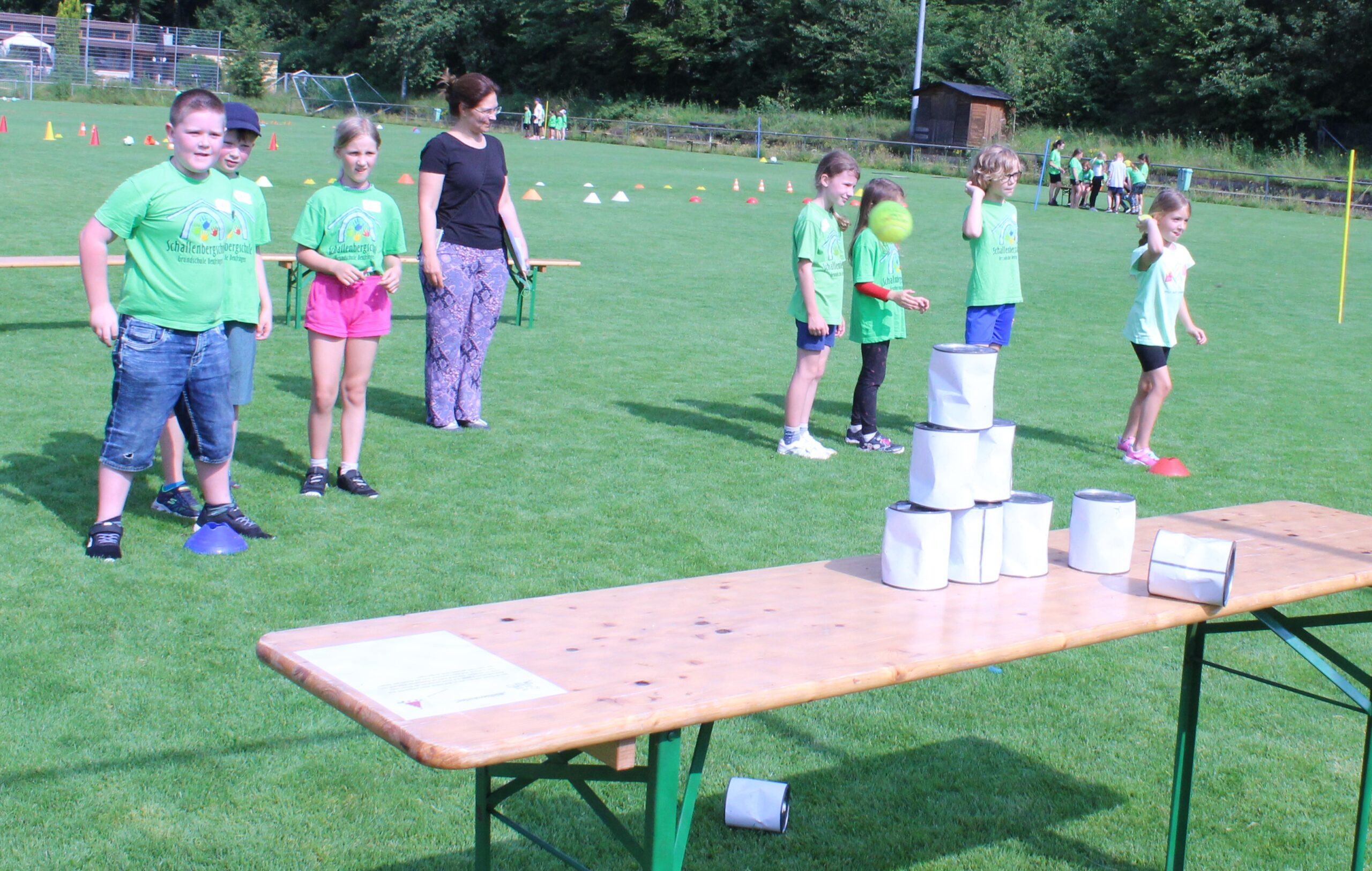 Kinder werfen mit Tennisbällen auf einen Turm aus Büchsen.