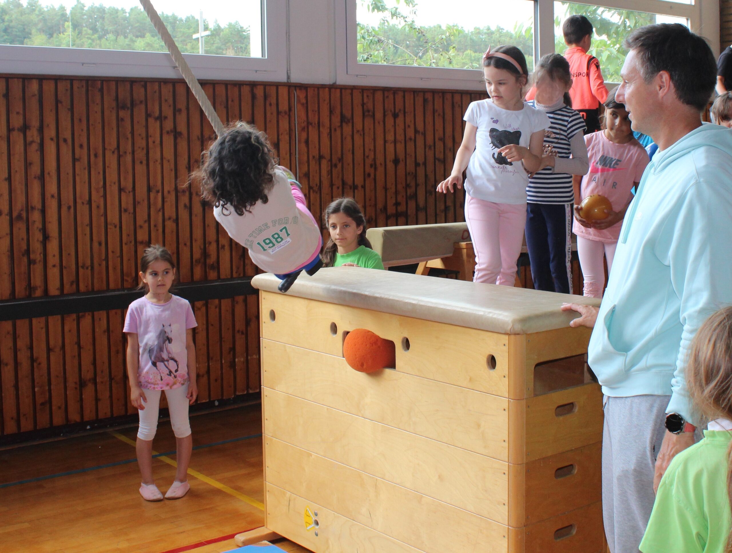 Kindergartenkinder schwingen an einem Tau von einem hohen Kasten aus.