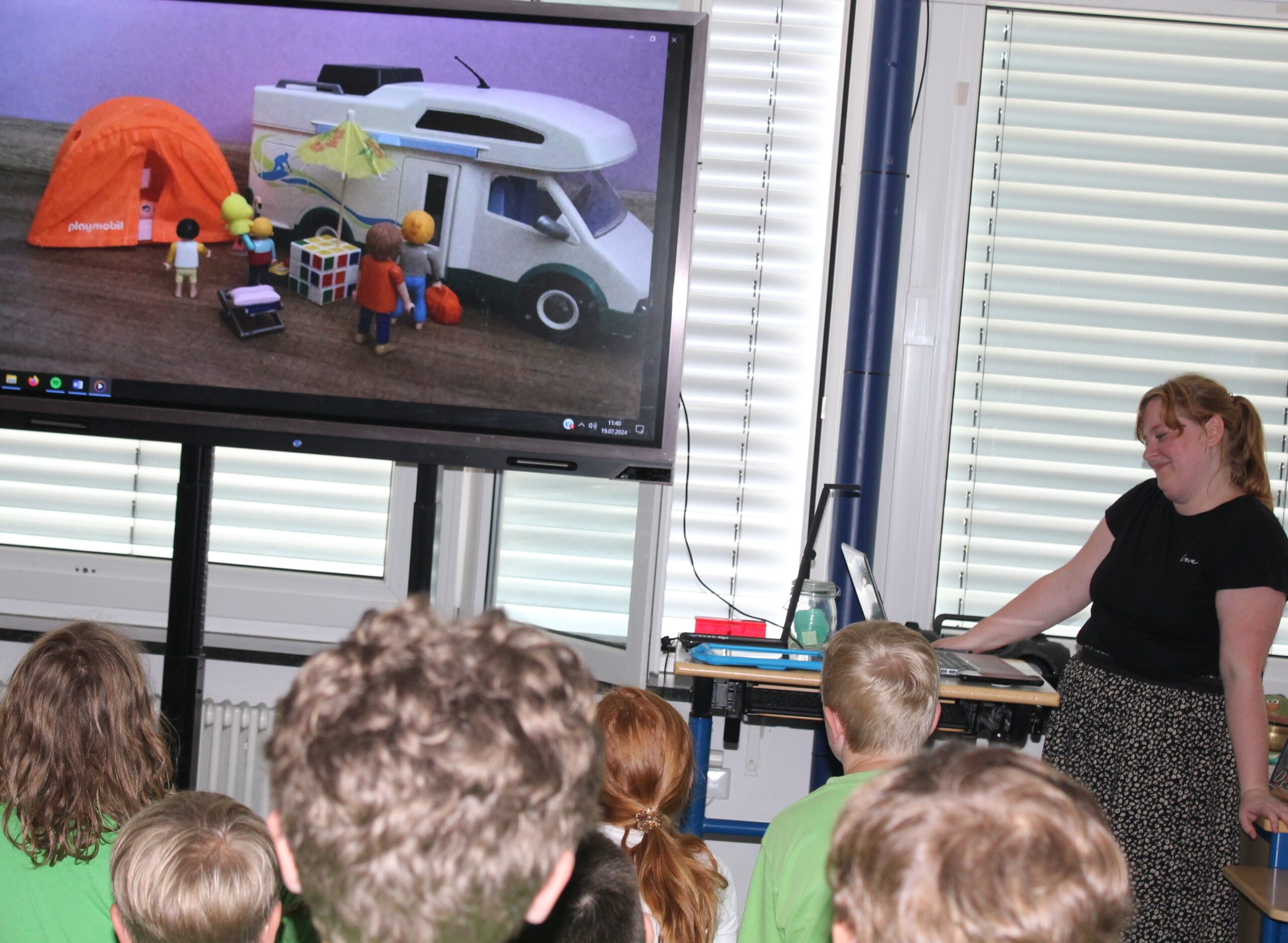 Kinder schauen in einem Klassenzimmer auf einem Panel einen Trickfilm an.