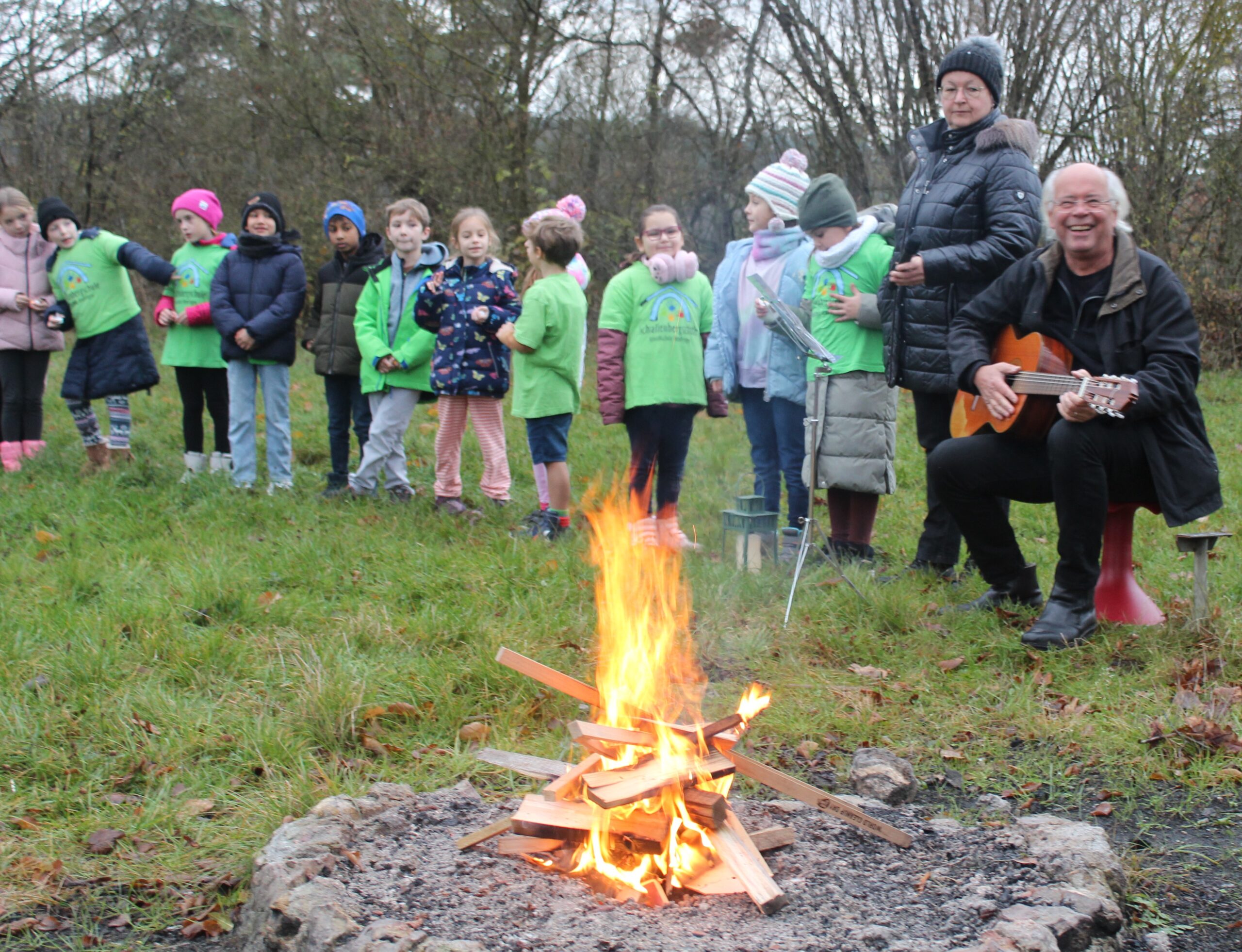 Ein Lehrer spielt Gitarre, und Kinder singen am Feuer dazu.