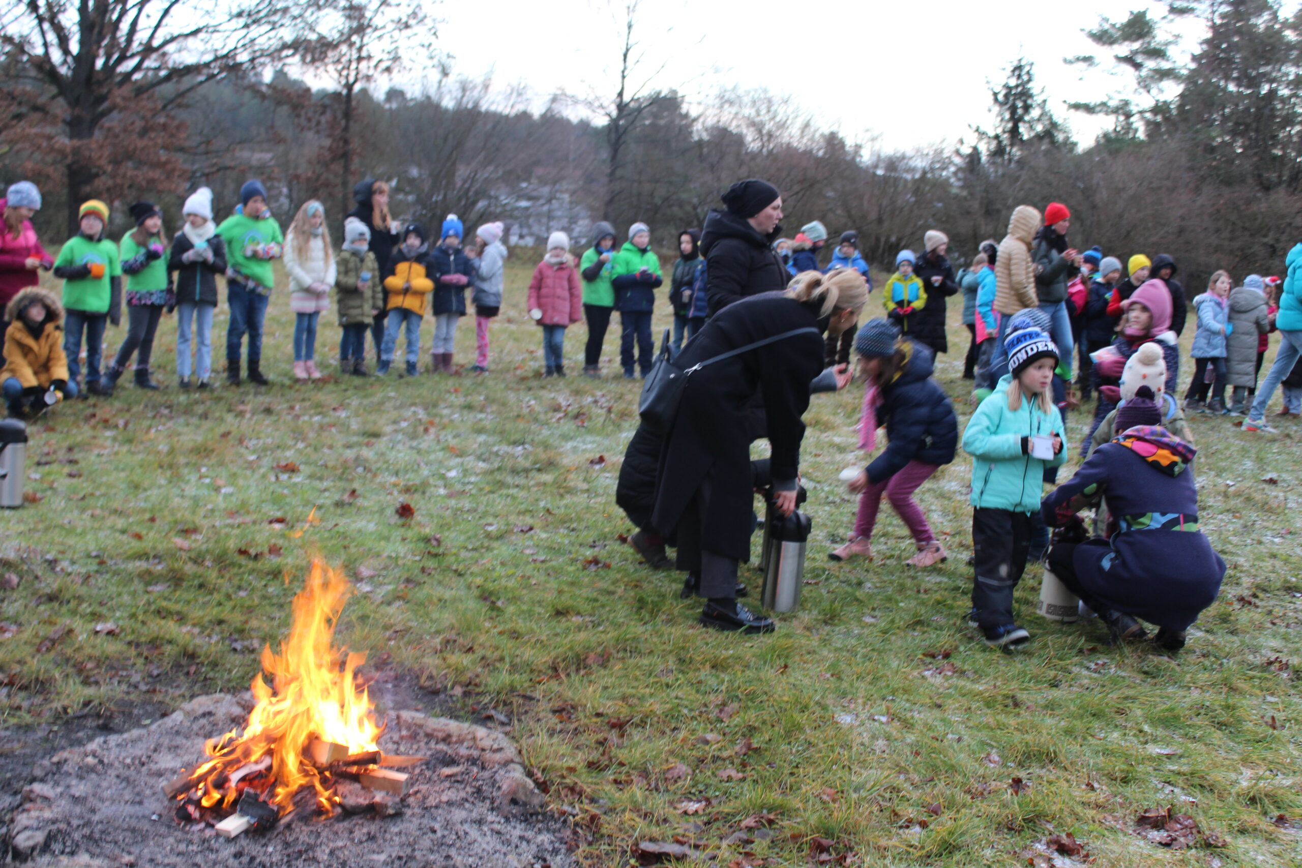 Eltern verteilen Punsch an Kinder vor dem Feuer.