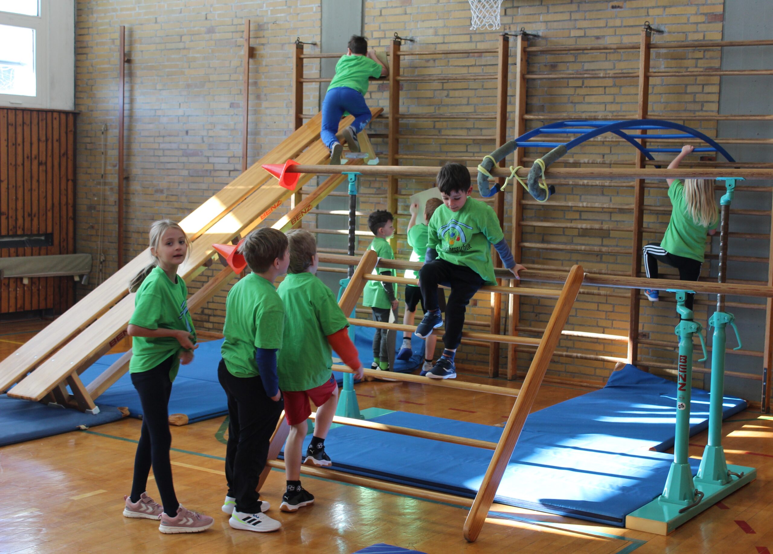 Bänke, die in der Sprossenwand eingehängt sind, ergeben für die Kinder in der Sporthalle eine Rutsche.