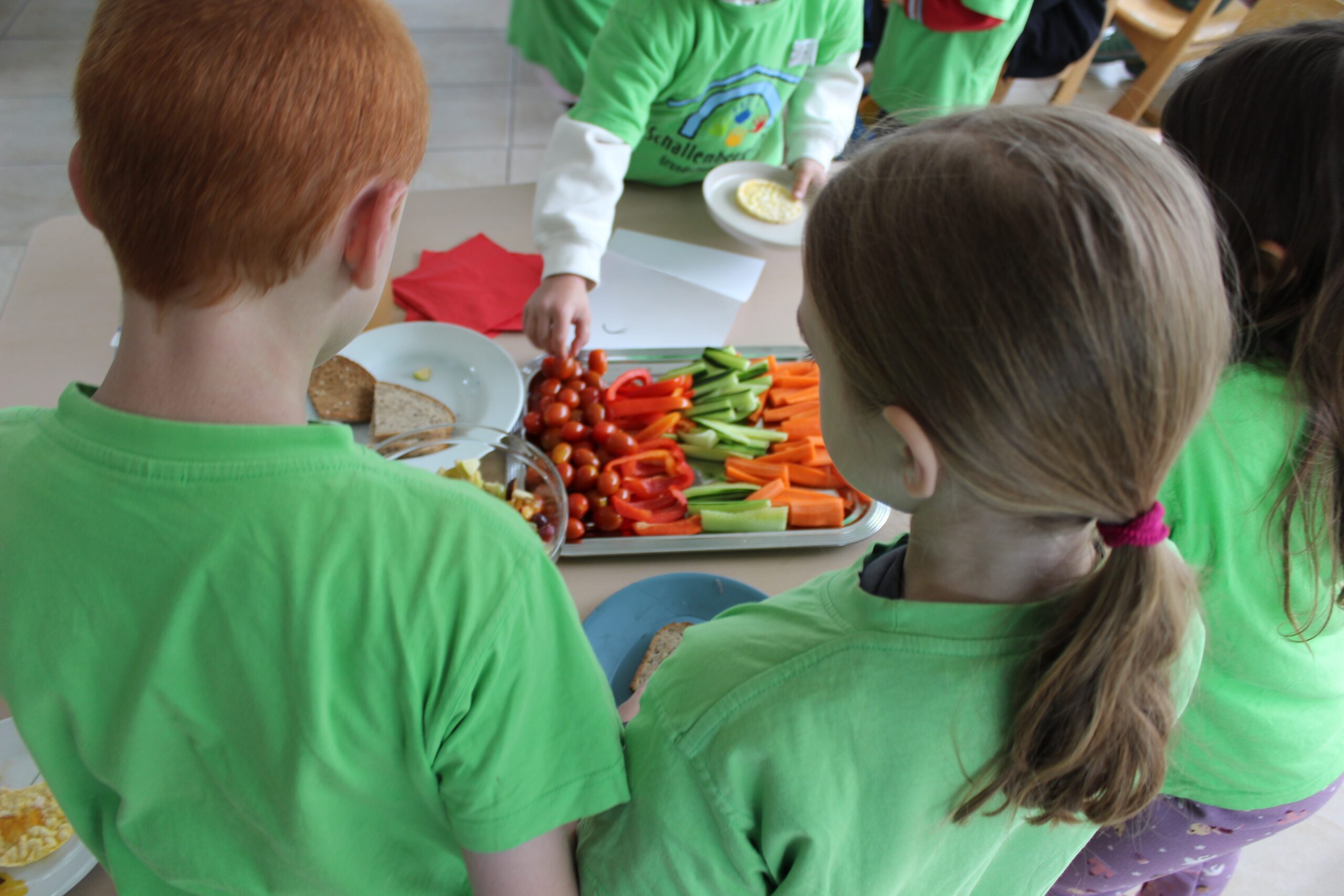 Die Kinder stehen an den Tischen mit dem frischen Gemüse.
