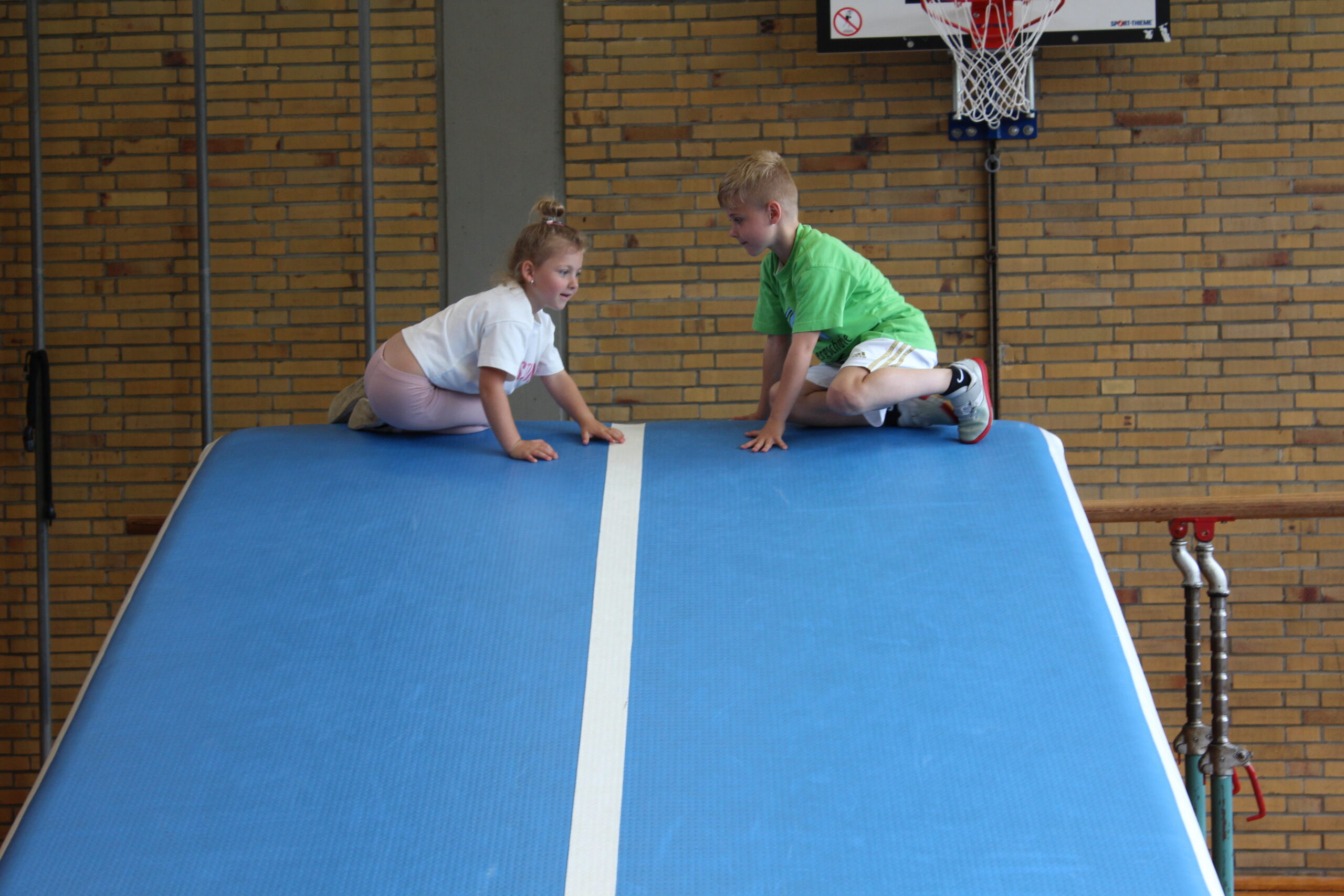 Ein Kindergartenkind und ein Pate sitzen auf einer schrägen Matte und bereiten sich vor hinunter zu rollen.