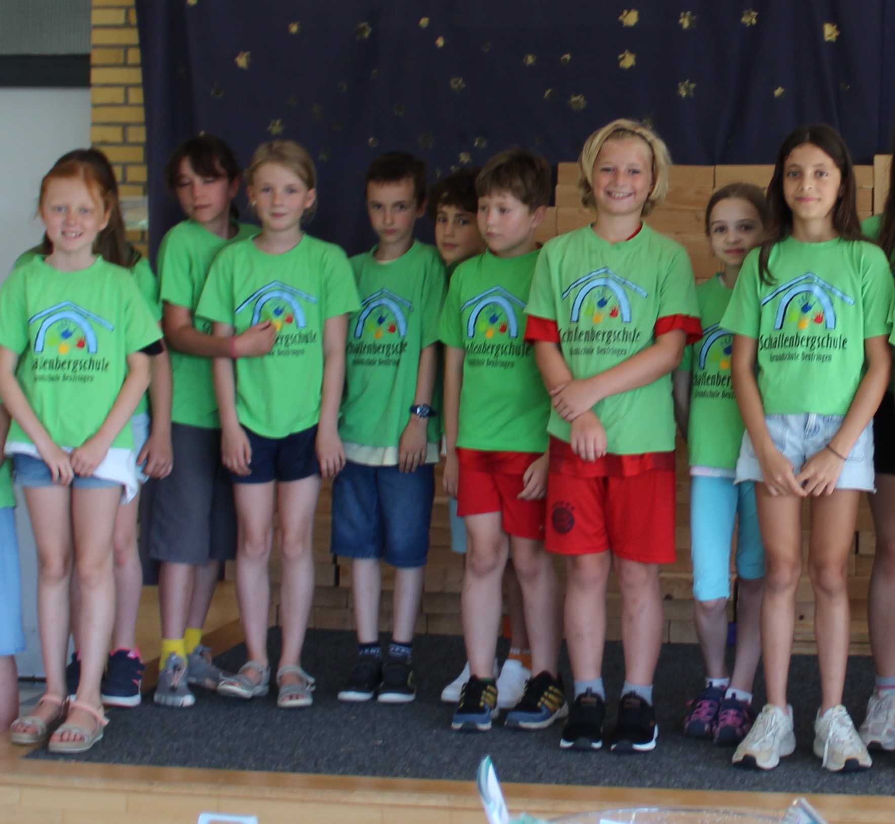 mehrere Kinder, auf einer Bühne, sie tragen das grüne Schalli T-Shirt