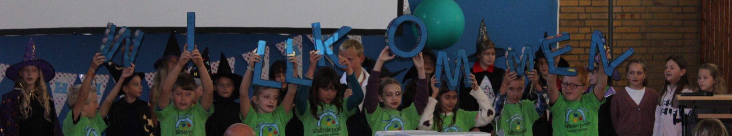 Abschlussbild des Theaterstücks. Alle Kinder halten Buchstaben hoch für Willkommen.