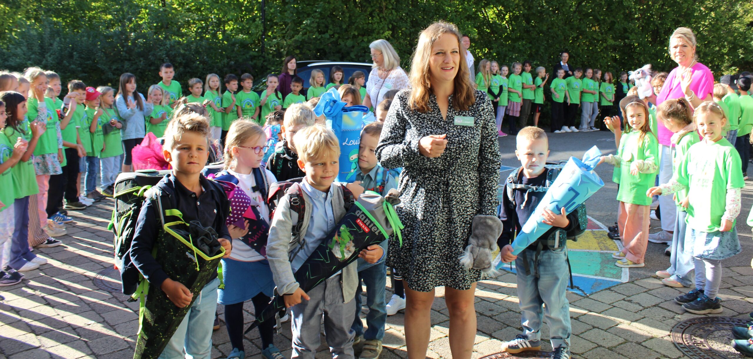 Die Lehrerin Frau Wipf wird mit ihrer Klasse vor der Schule von allen anderen Kindern begrüßt und sie gehen zur ersten Unterrichtsstunde ins Schulhaus.