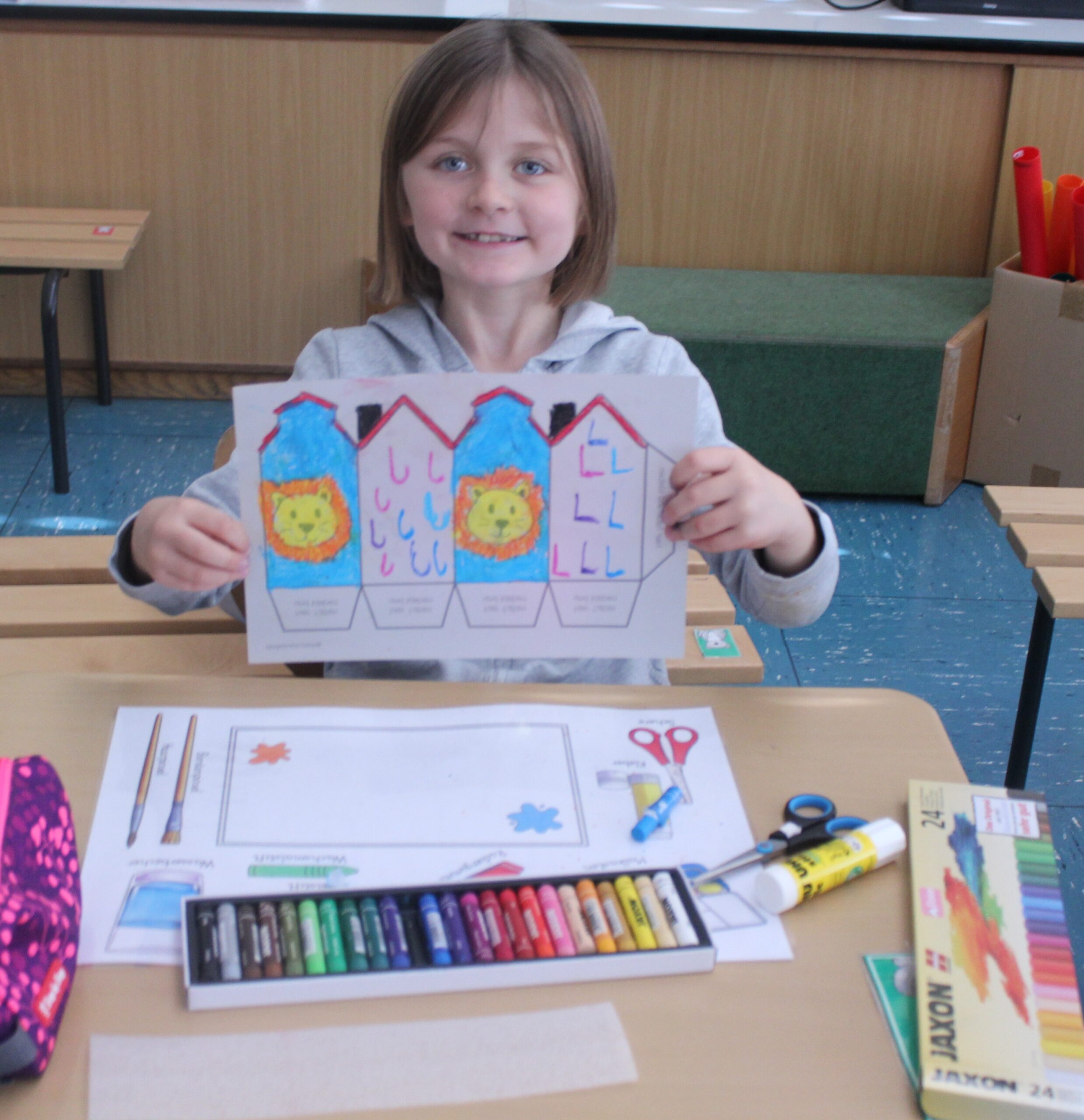Ein Mädchen hält ein Transparentbild in die Kamera, das mit Jaxson Kreide bemalt ist und zu einer Laterne gebastelt werden kann.