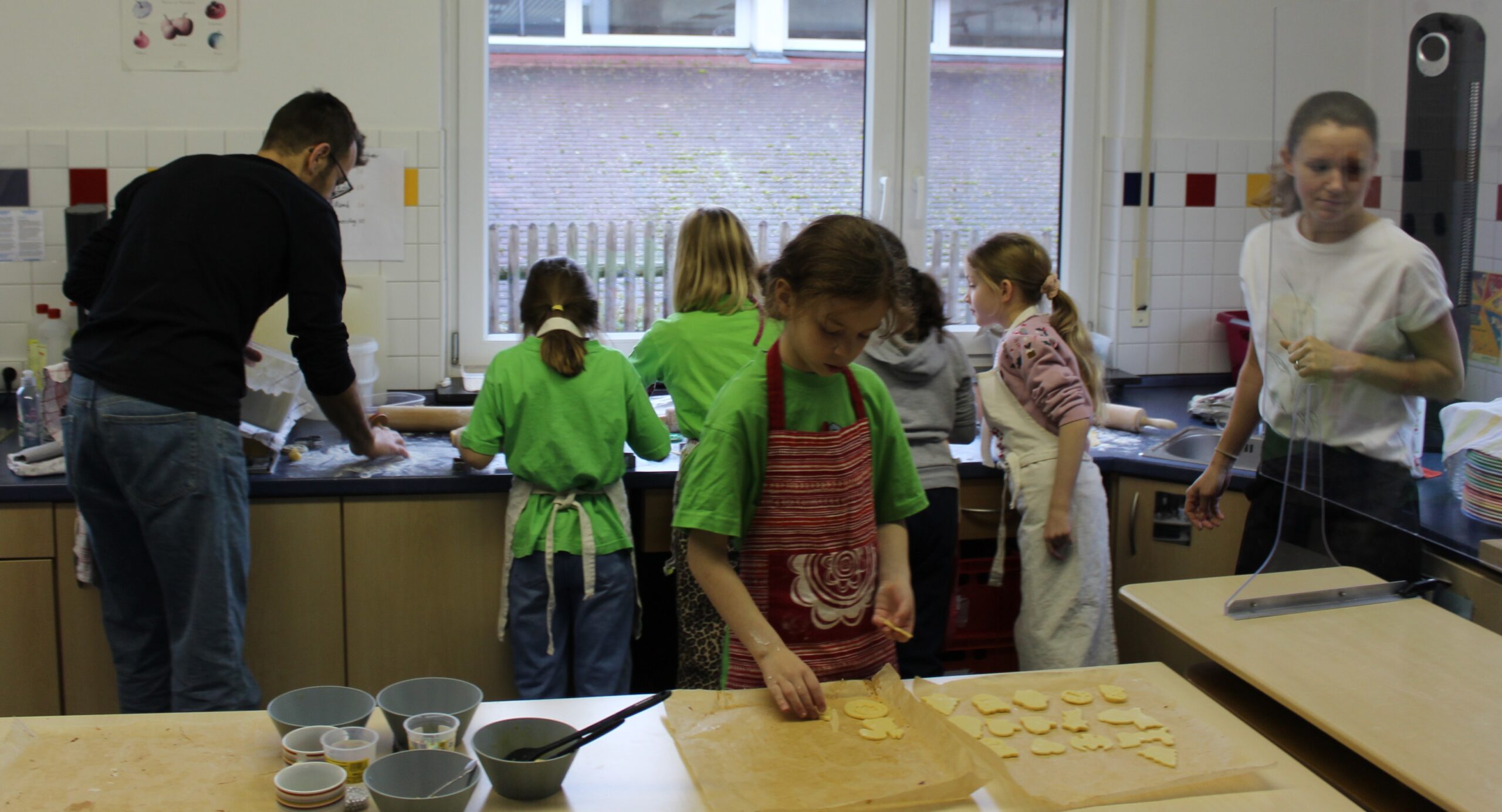 Kinder backen in der Schulküche Weihnachtsplätzchen und dekorieren sie mit verschiedenen Zuckerkugeln.