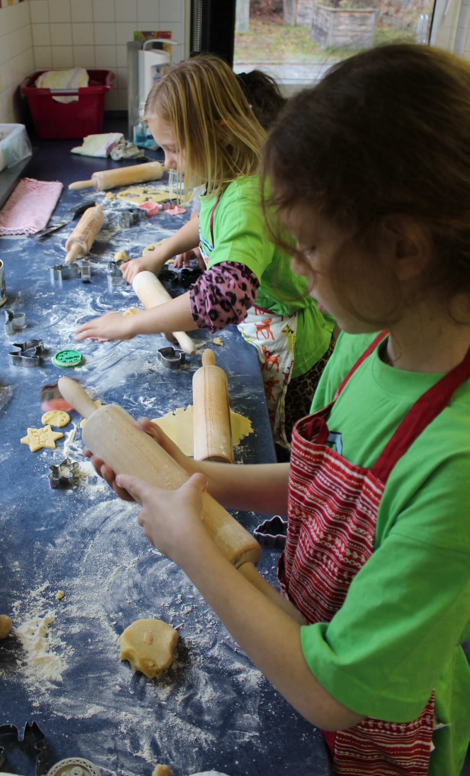 Kinder rollen den Teig in der Schulküche aus und stechen Plätzchen aus.