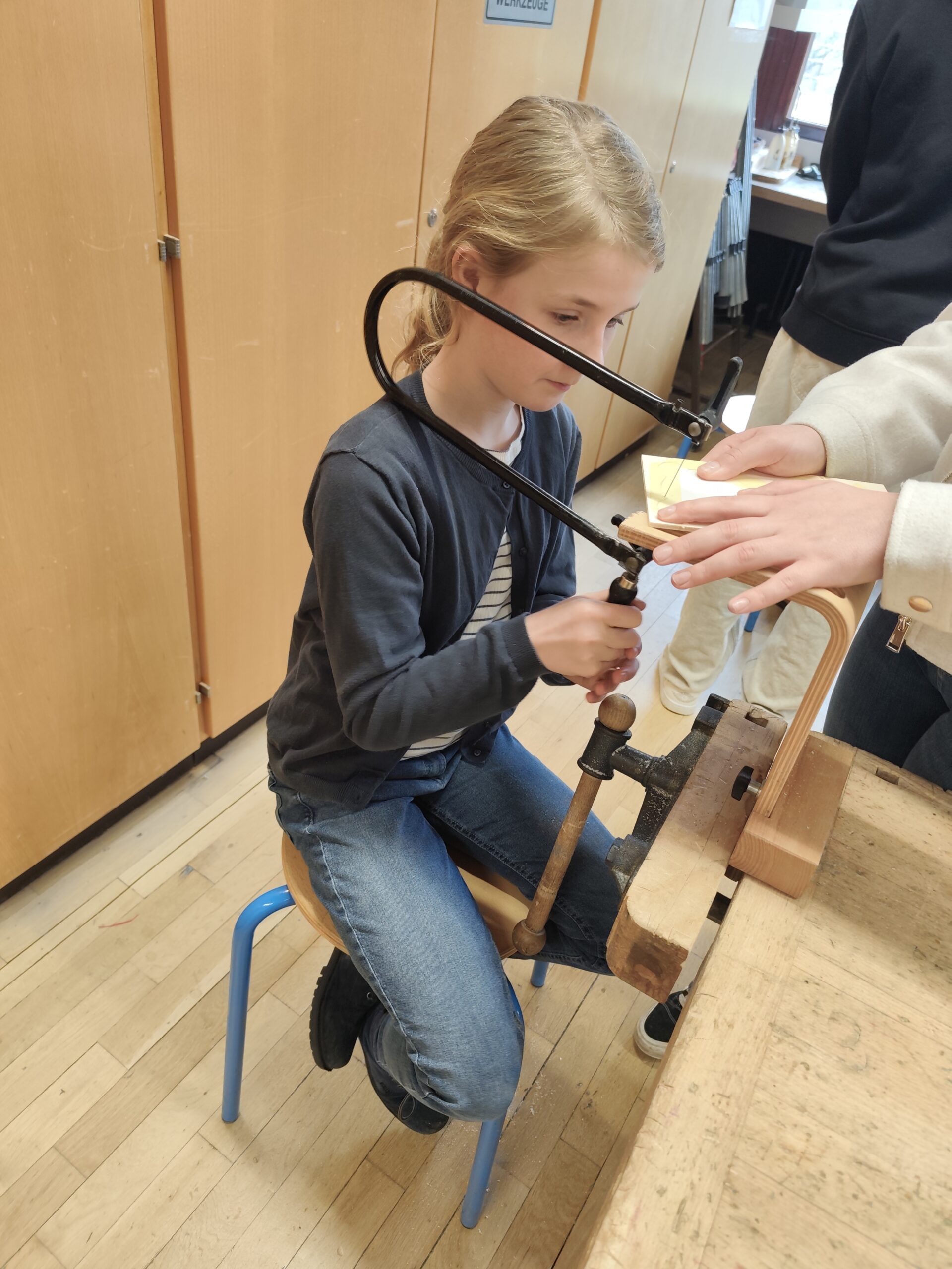 Ein Mädchen sägt mit einer Laubsäge.