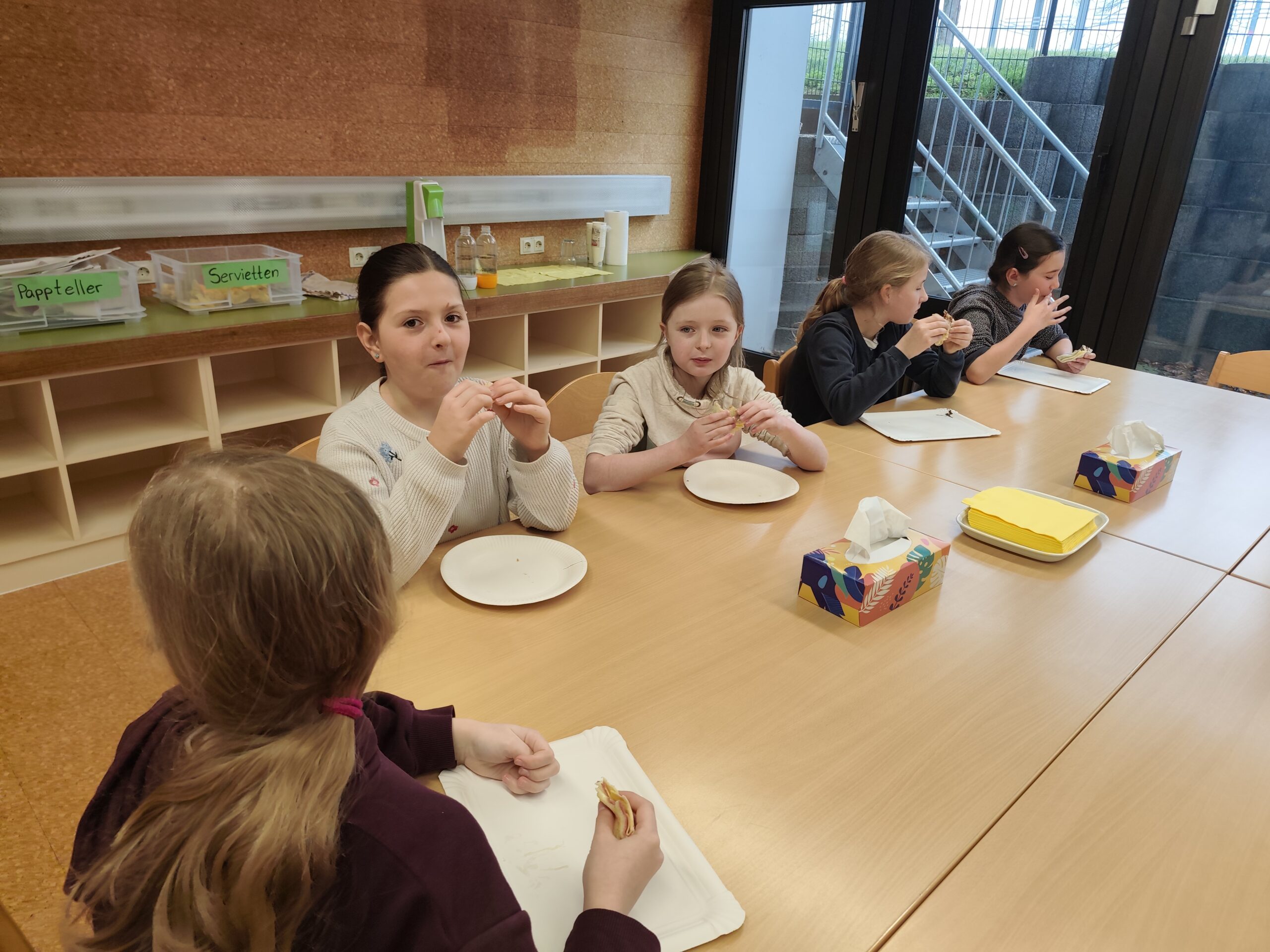 Kinder sitzen essend um einen Tisch in der Schulküche.