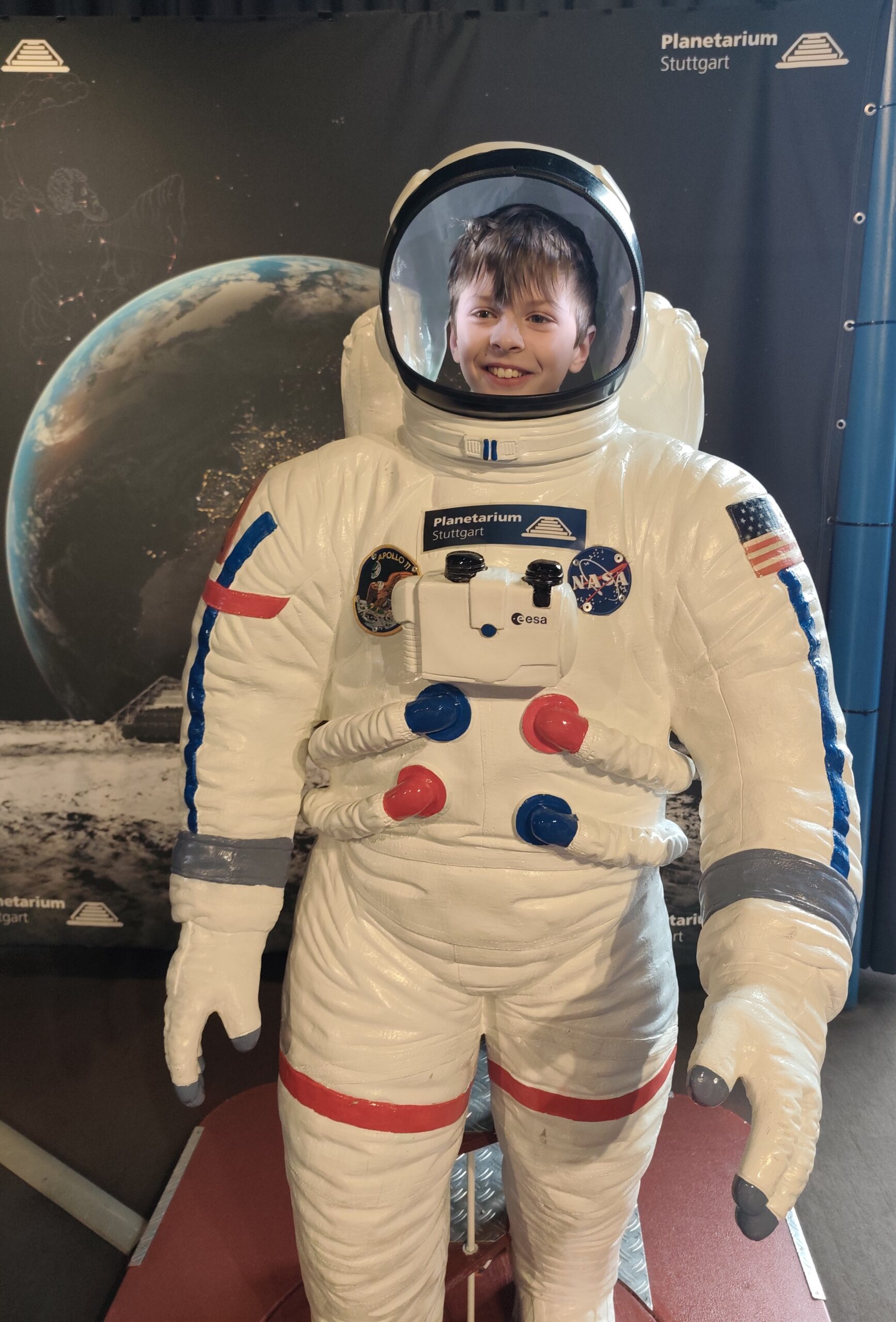 Ein Kind steht hinter einem Raumanzug und sieht so aus, wie ein Astronaut.
