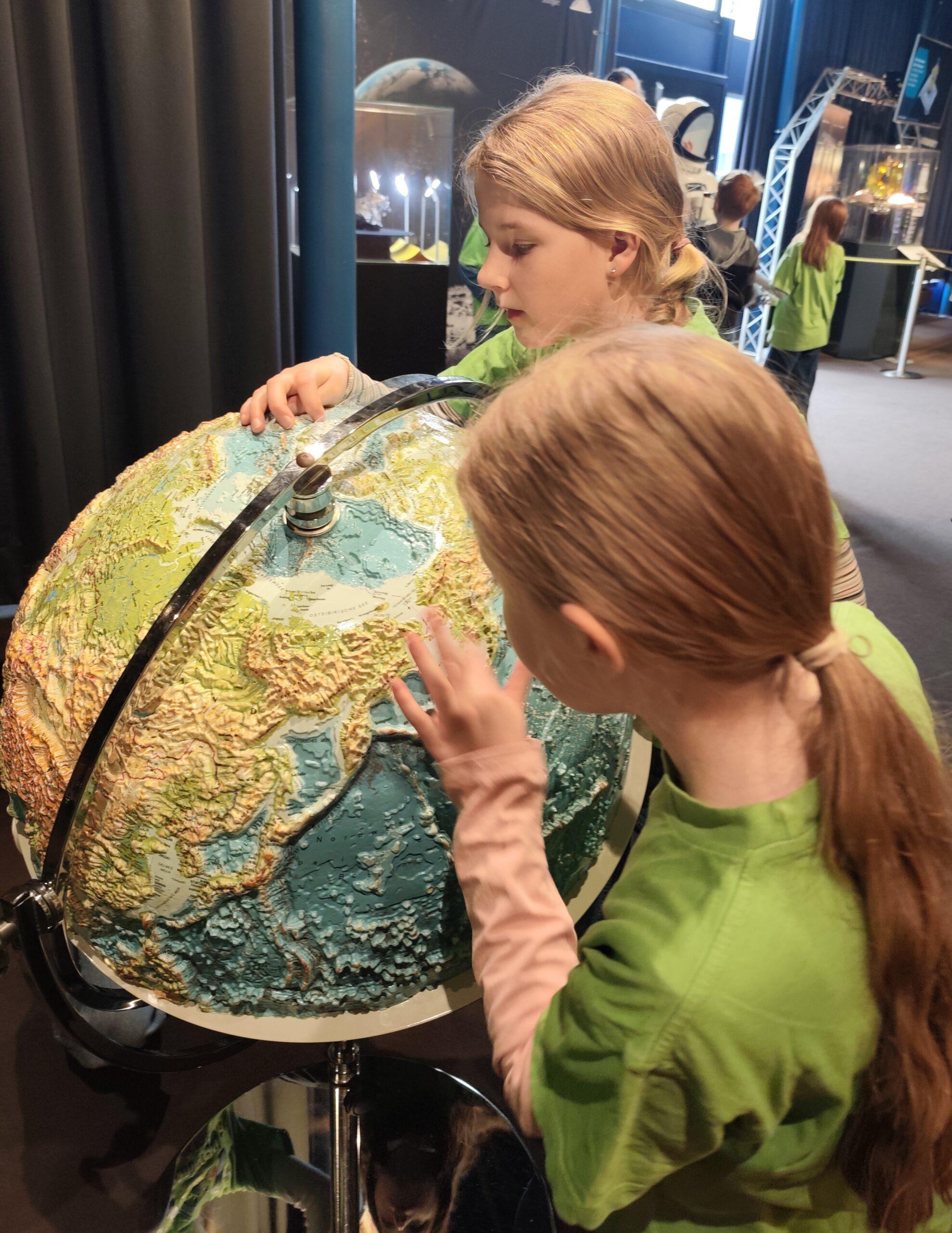 Zwei Kinder schauen im Planetarium eine Erdkugel genau an.