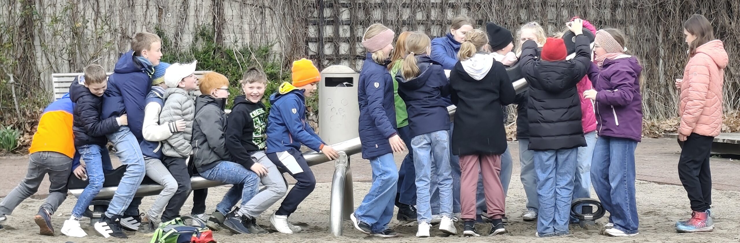 Eine Schulklasse spielt auf einer Wippe an einem Spielplatz.