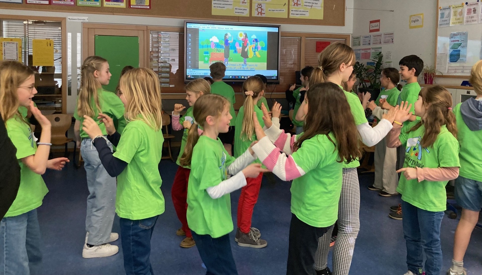 Die Kinder einer Schulklasse singen und tanzen zu einem Freundschaftslied.
