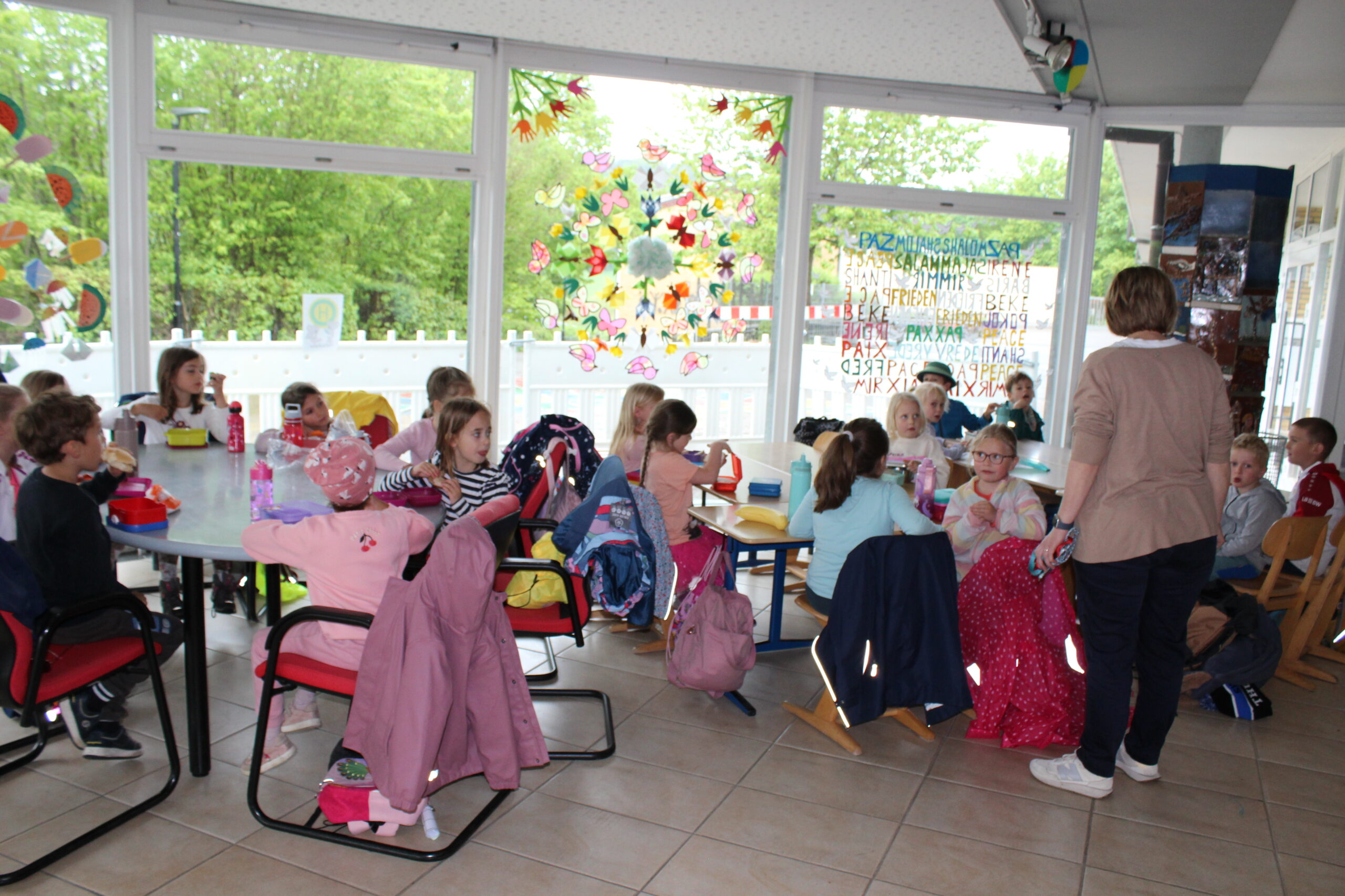 Die Kindergartenkinder vespern in der Aula und die Kooperationslehrerin spricht mit ihnen.