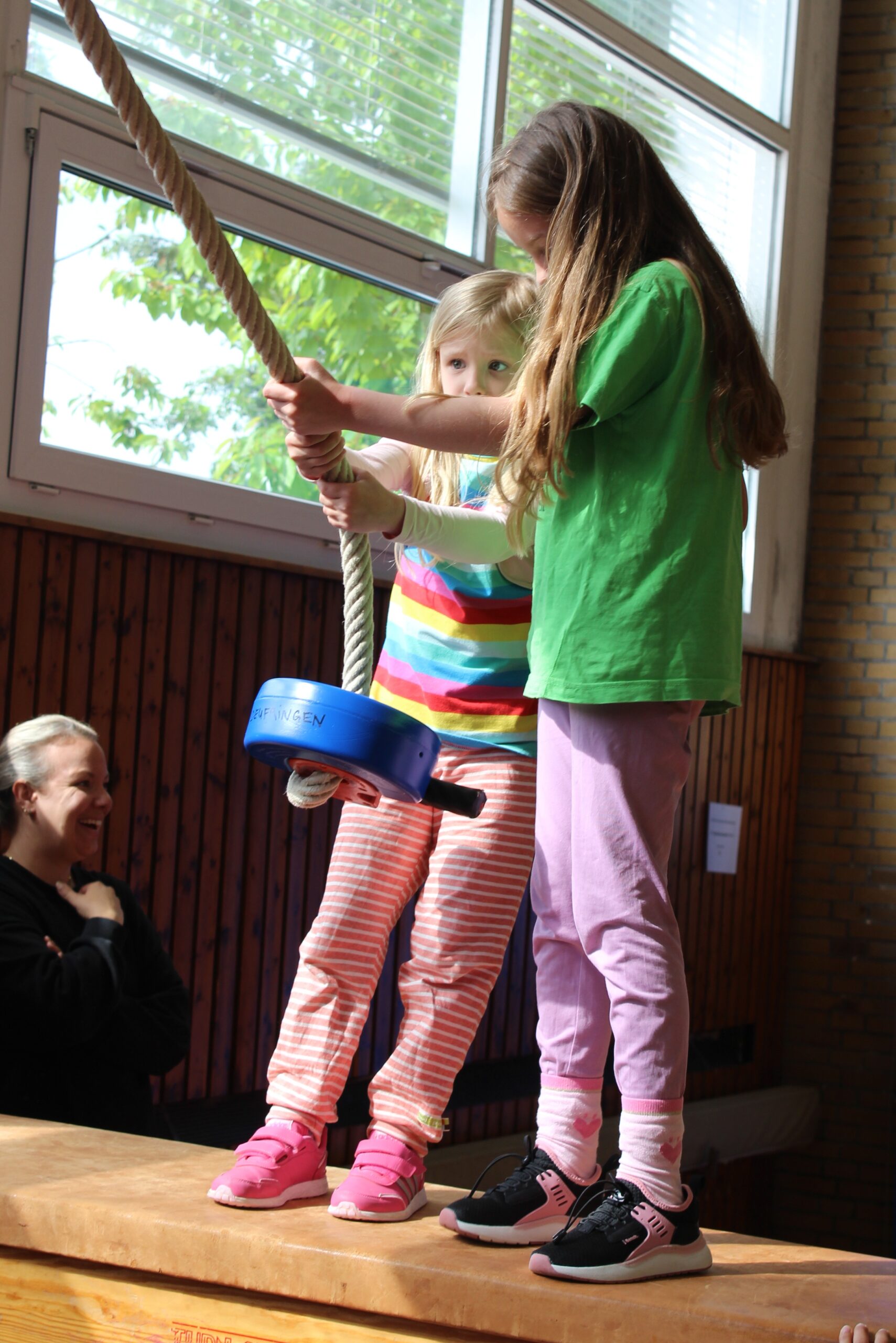 Eine Drittklässlerin hält einem Kindergarten das Tau hin zum Schwingen.