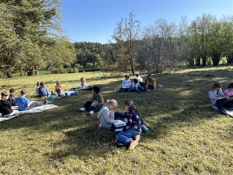 Kinder sitzen im Gras und lesen.