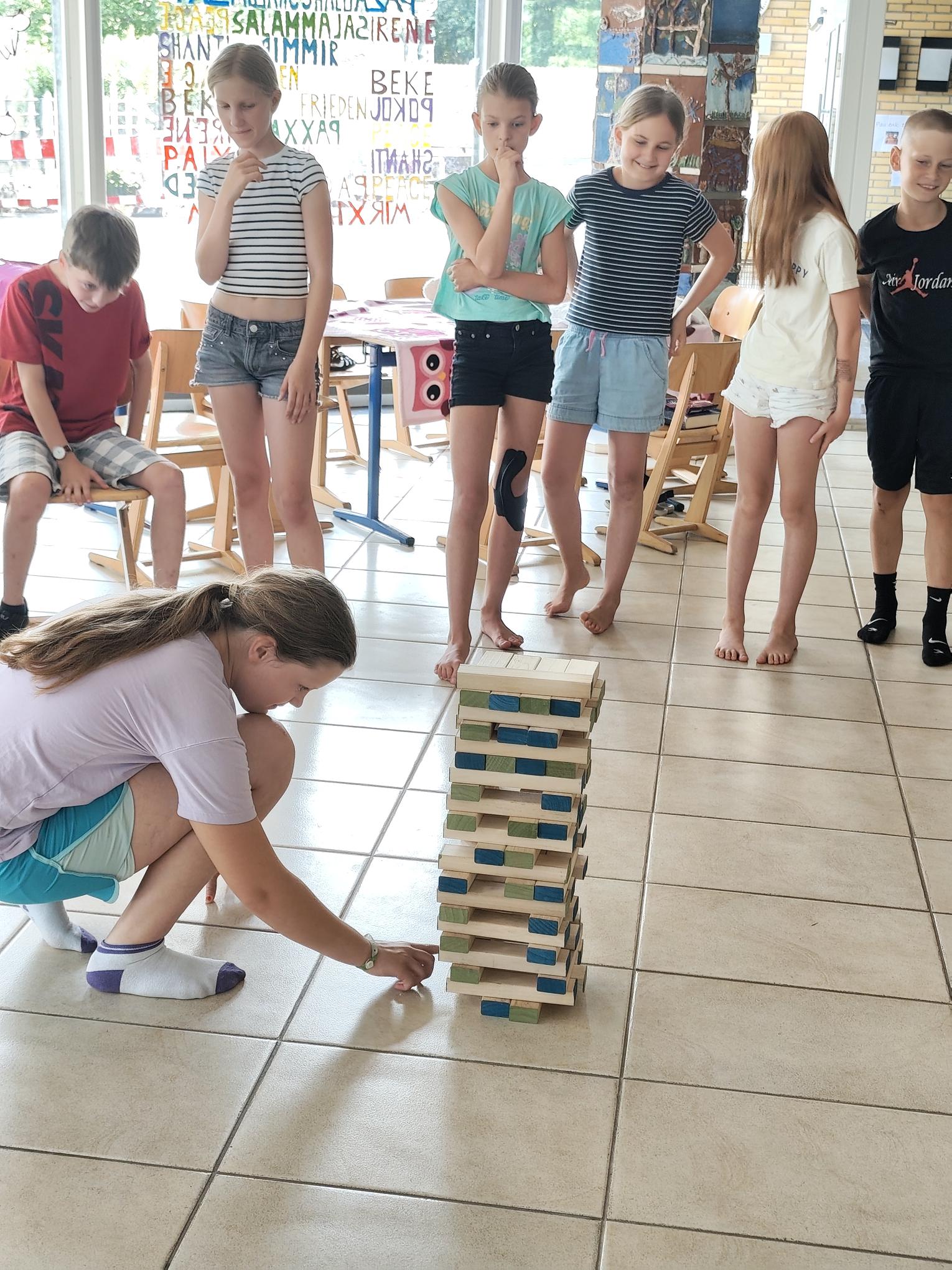 Kinder bauen in der Schulaula einen Turm aus Holzkötzchen.
