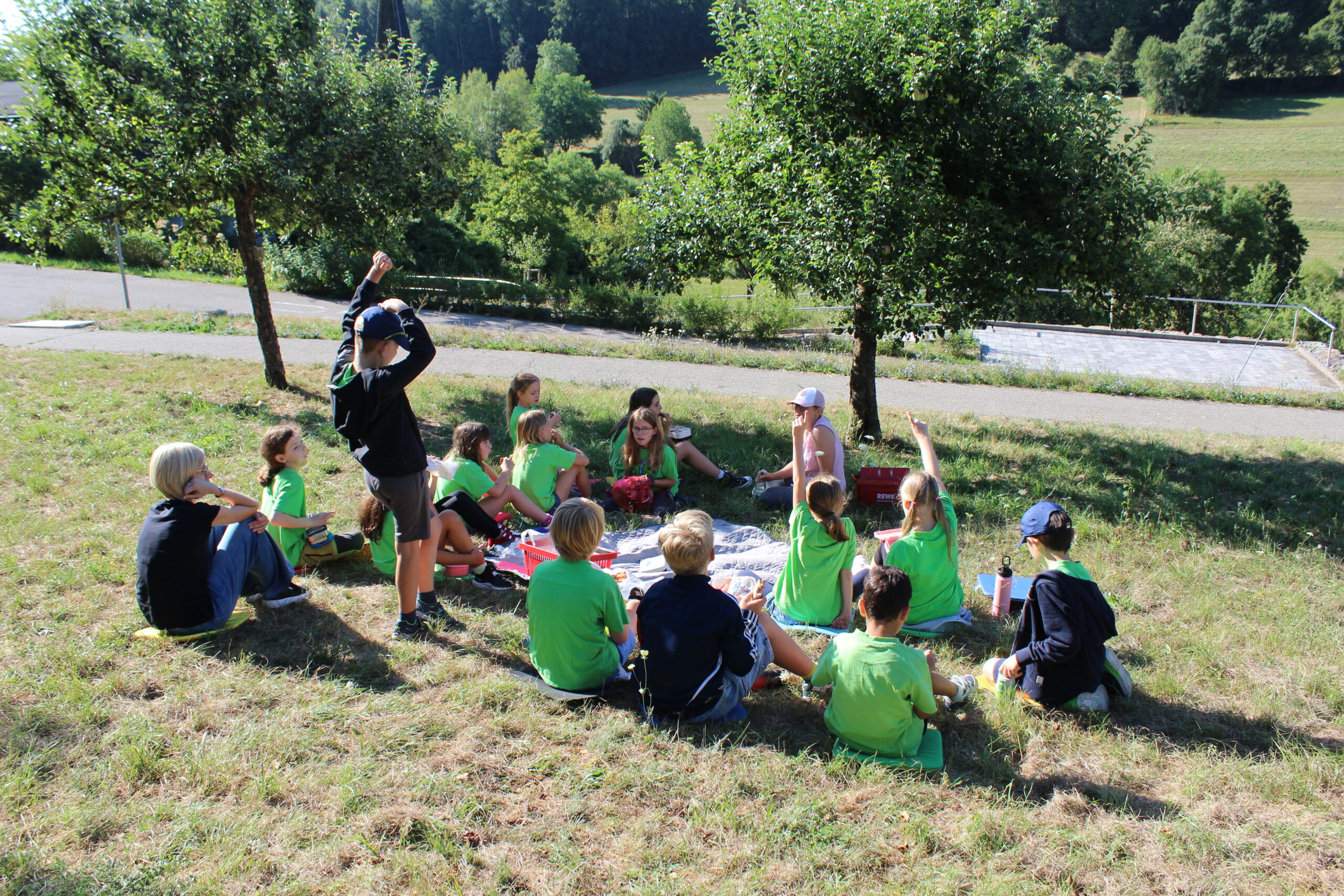 Die Schulklasse sitzt auf der Wiese und die Streuobstpädagogin unterrichtet sie.