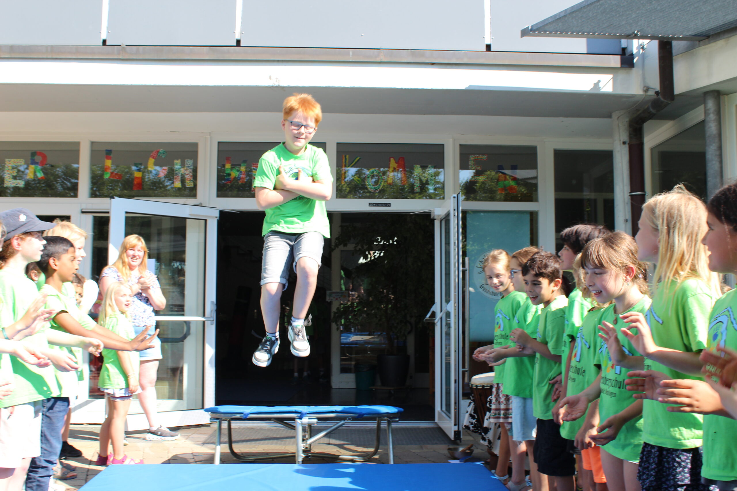 Ein Junge springt in ein Trampolin vor der Schultüre und "fliegt" somit aus der Schule.